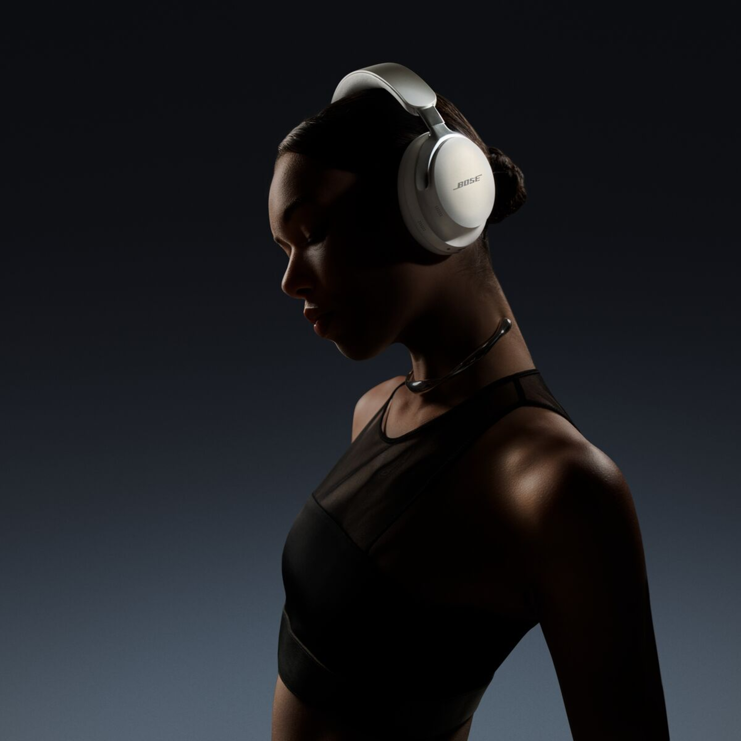 Une femme portant un casque Bose blanc, dans un environnement sombre. Effet de silhouette sur fond bleu foncé.