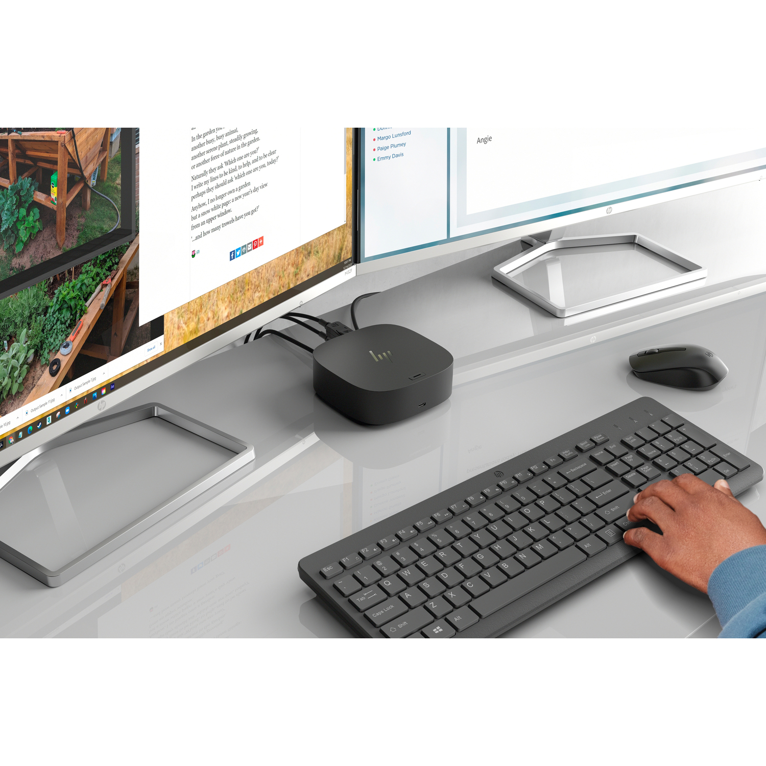 Een werkruimte met monitoren, een toetsenbord, een muis en een zwarte hub op een glazen bureau.