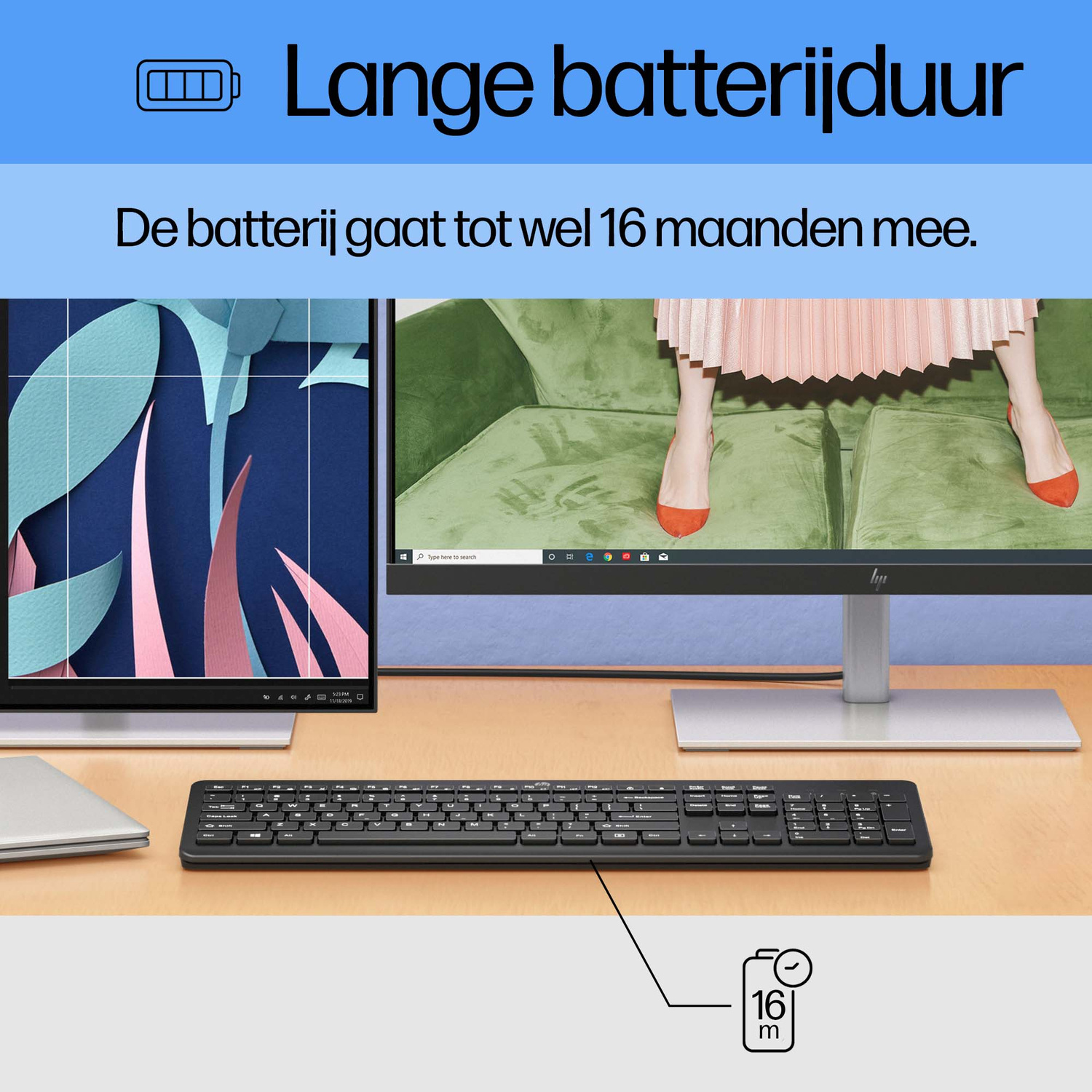 Monitor, keyboard, and laptop on a wooden desk. Text: Long battery life. Woman in the background, orange shoes.