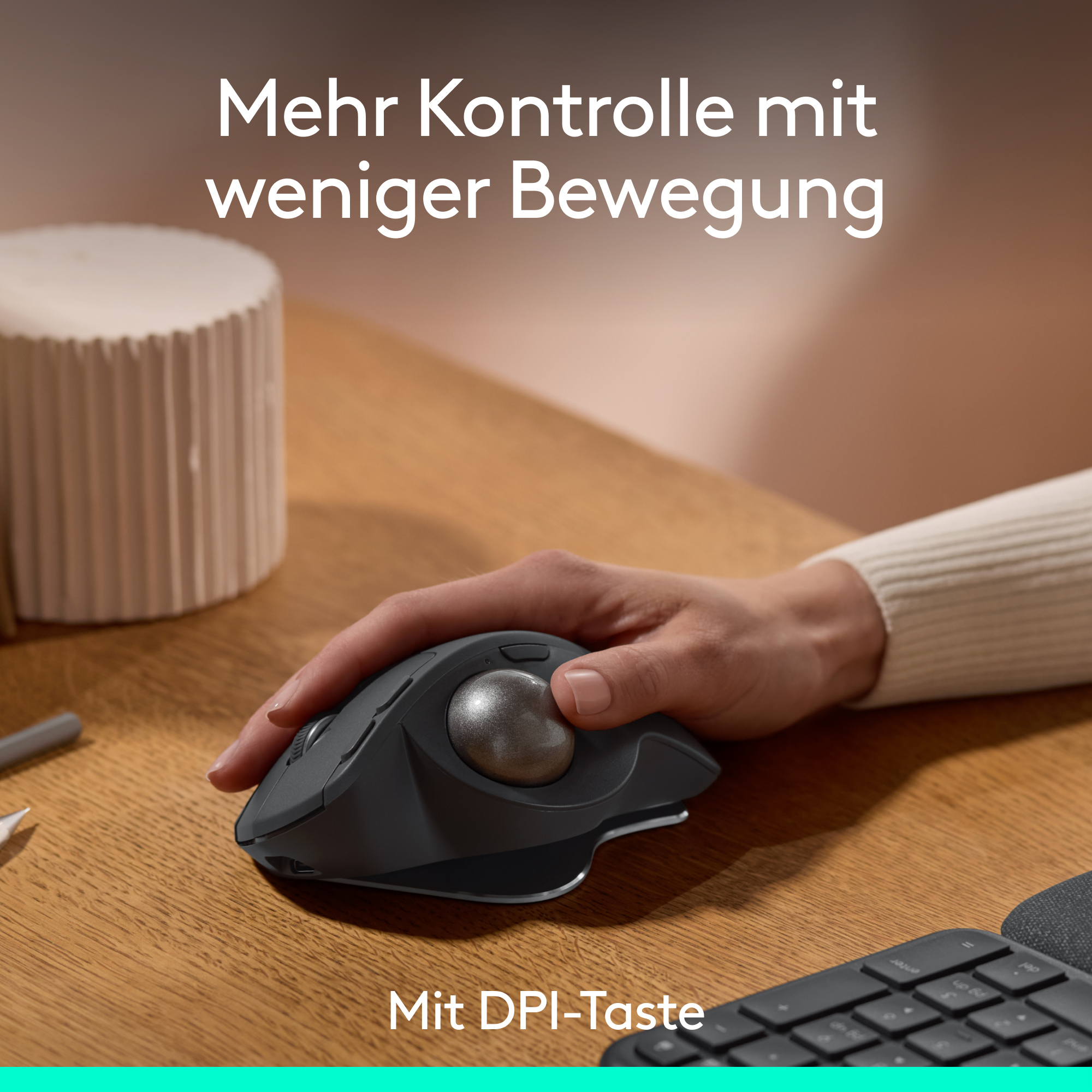 Hand benutzt eine Trackball-Maus auf einem Holztisch mit einem weißen Zylinder und Text darüber.