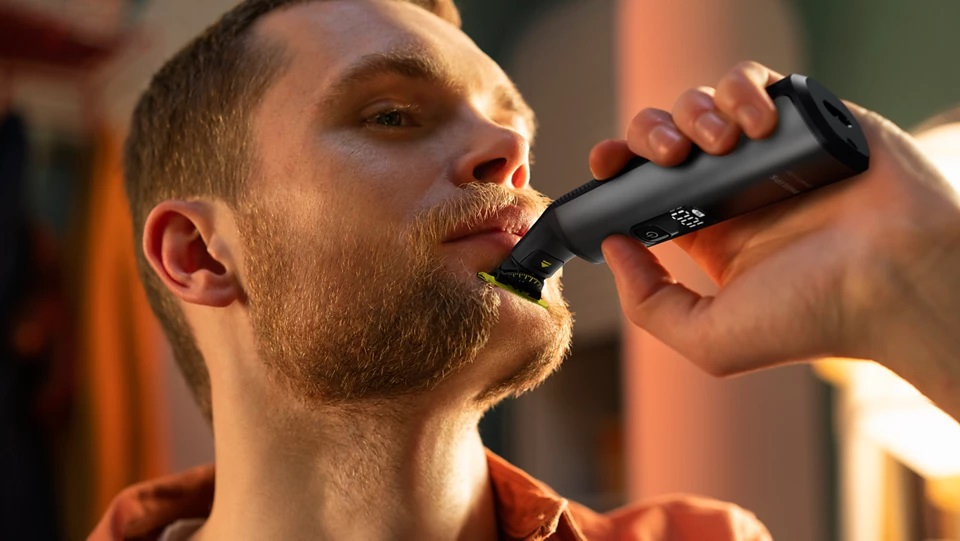 Mężczyzna goli brodę golarką elektryczną; zbliżenie na jego twarz.