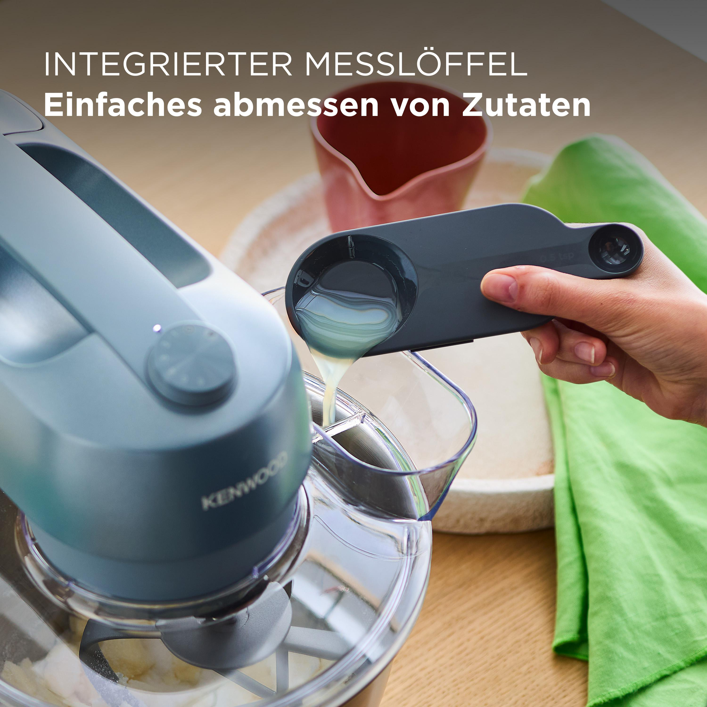 Ein Küchengerät mit Messlöffel, der Flüssigkeit in die Schüssel gießt. Grünes Tuch und rosa Behälter im Hintergrund.