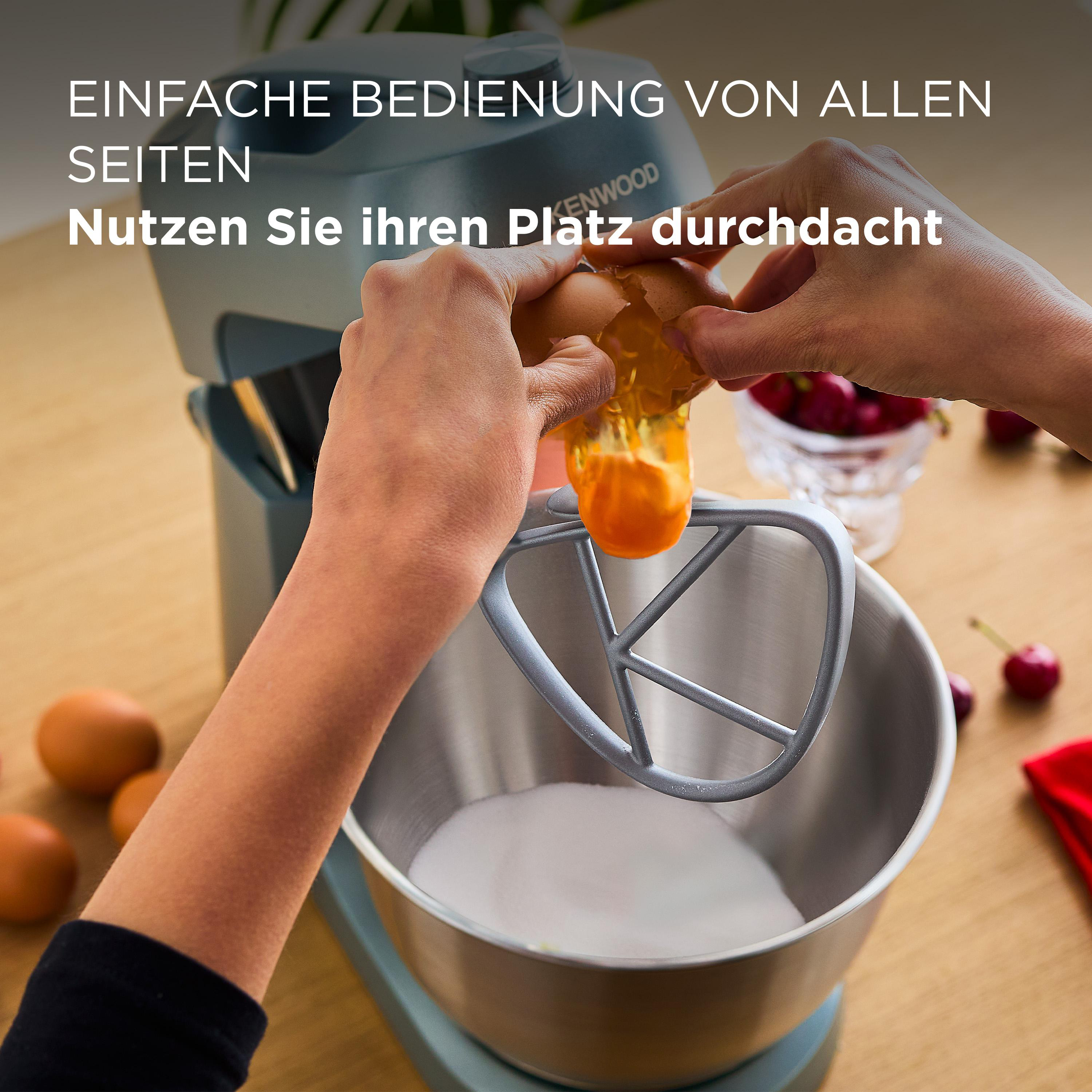 Hände, die ein Ei in einen Mixer mit Zucker aufschlagen. Kirschen liegen auf dem Tisch.