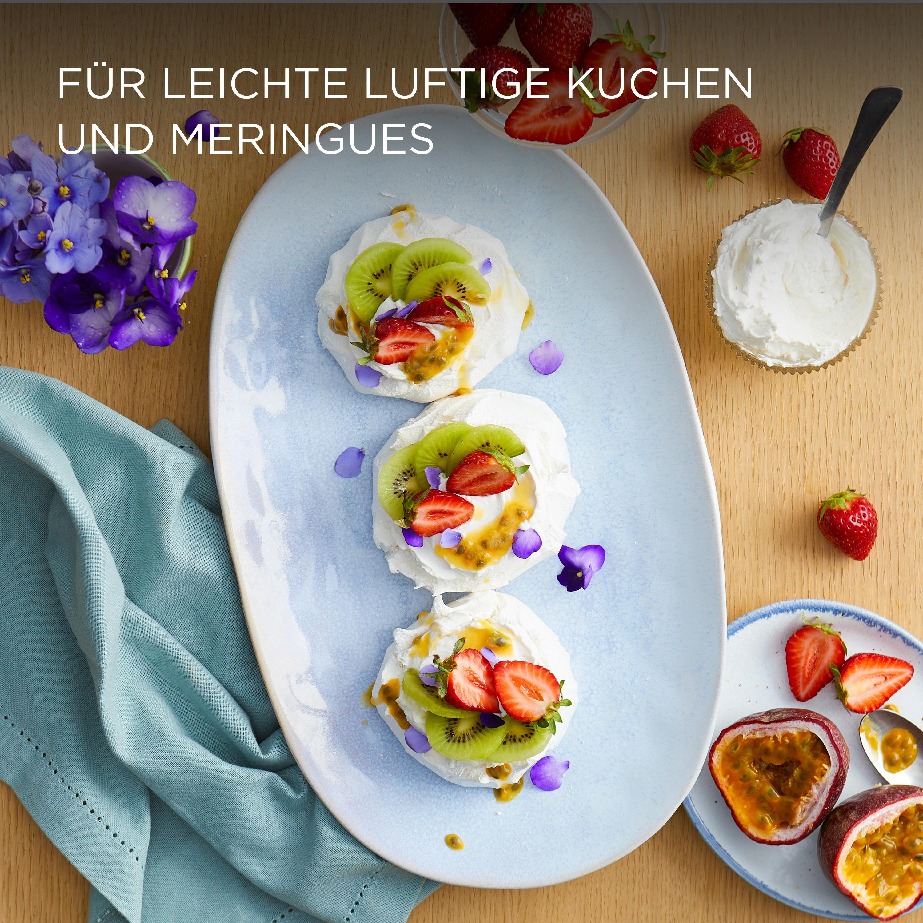 Pavlovas mit Kiwi und Erdbeeren auf einem blauen Teller. Erdbeeren, Sahne und Blumen sind ebenfalls vorhanden.