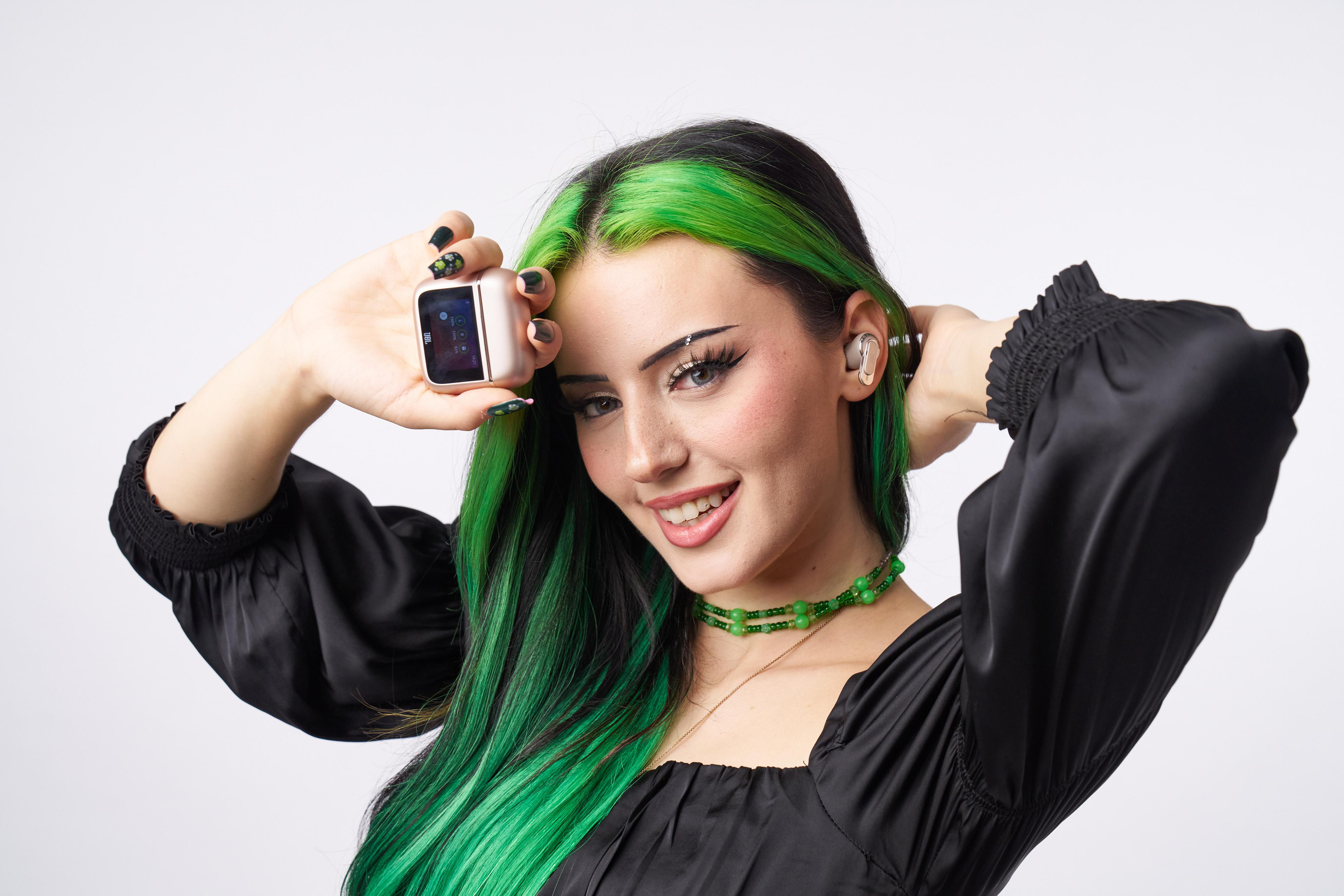 Eine Frau mit grünen Haaren hält eine roségoldene Apple Watch und Ohrhörer.