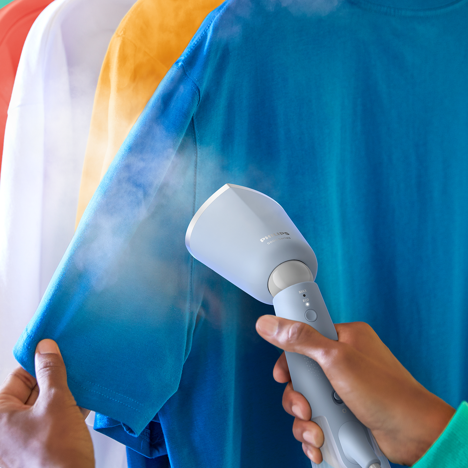 Een persoon die een blauw overhemd stoomt met een handstomer. Andere overhemden hangen op de achtergrond.