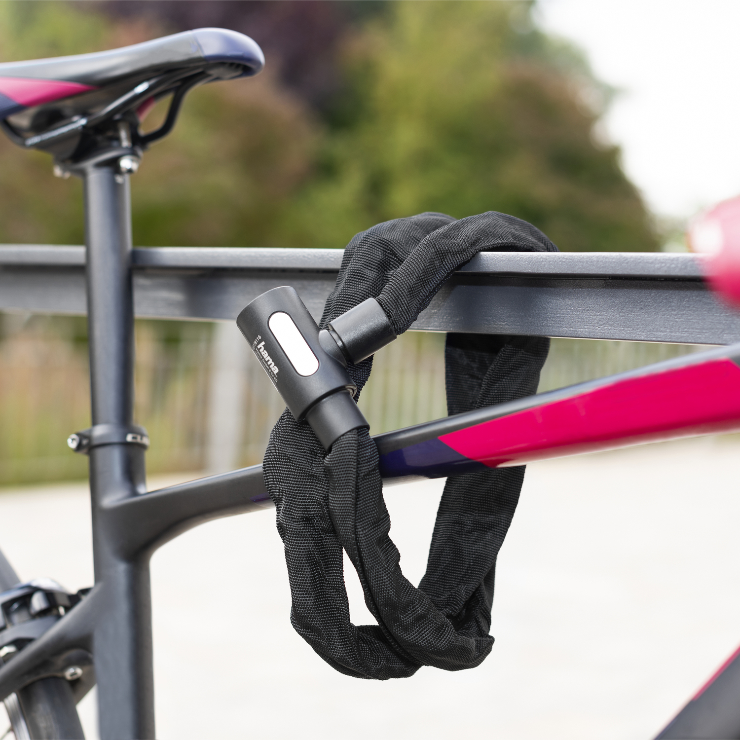 Een zwart fietsslot dat een fiets aan een metalen reling vastzet. Het slot is van ketting.
