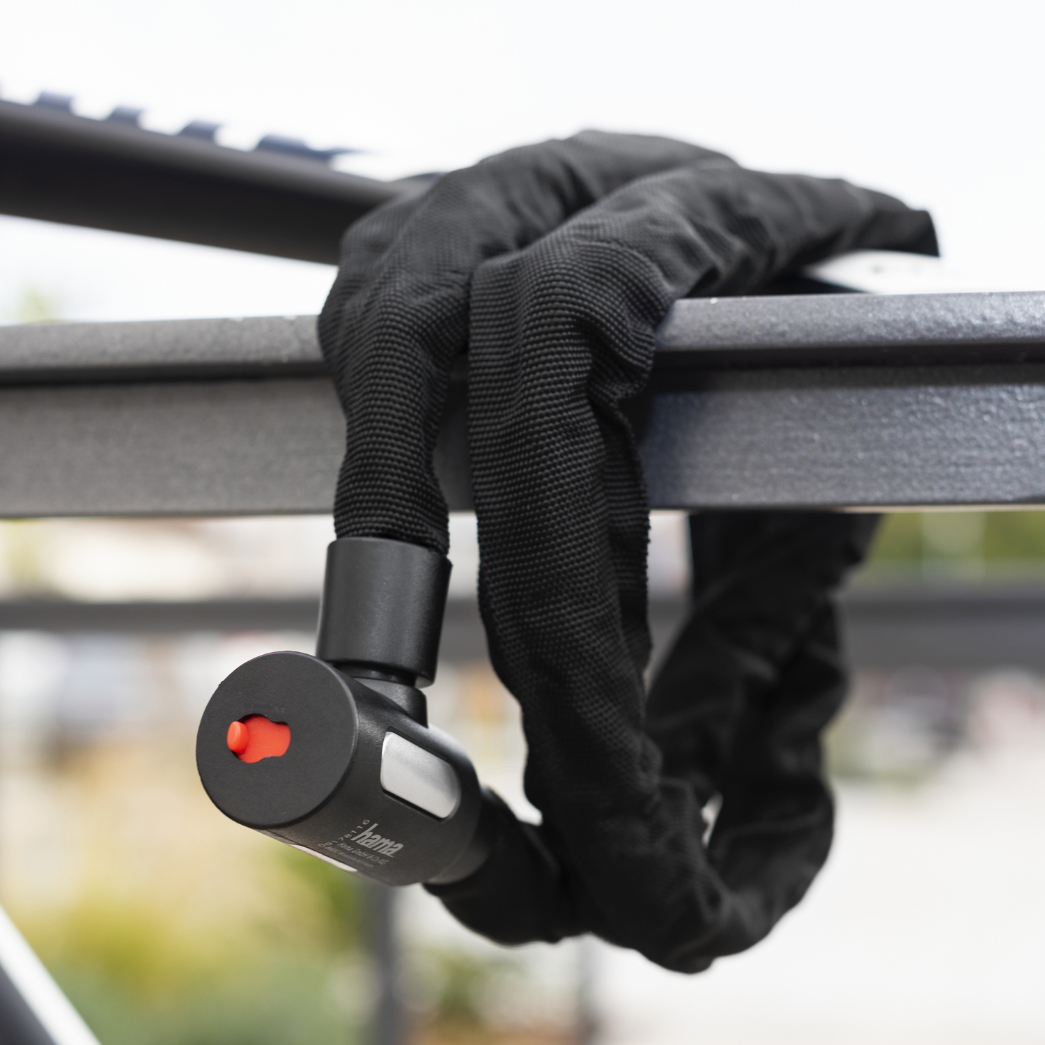 Een zwart kettingslot bevestigd aan een metalen stang. Het slot heeft een rode knop.