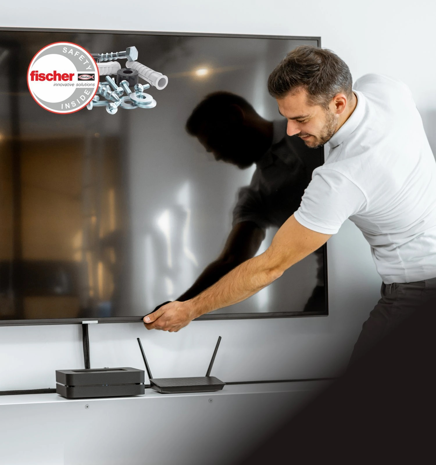 Mężczyzna instalujący telewizor, z logo i sprzętem fischer powyżej. Router i pudełko na półce.