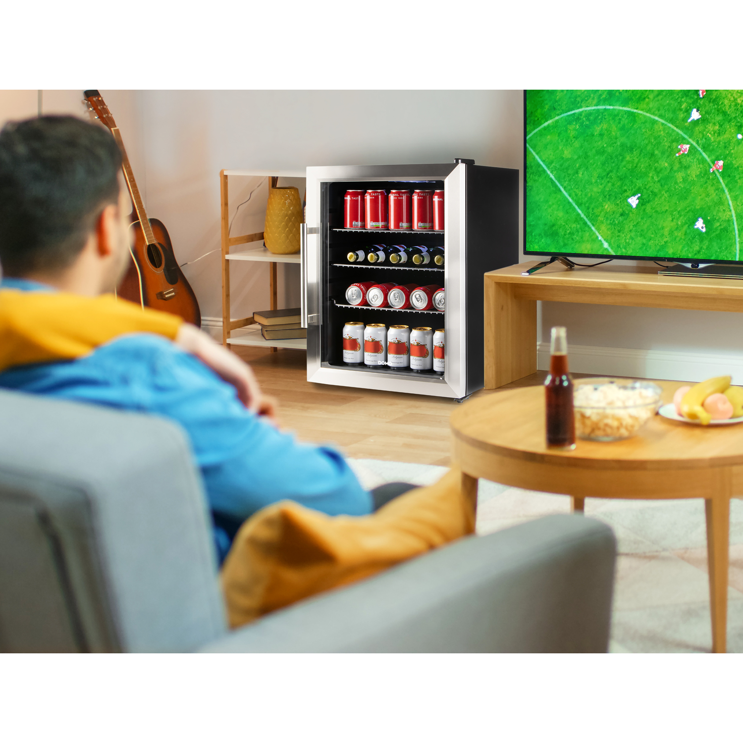 Scène de maison. Homme et femme assis, regardant la télé avec frigo, collation et guitare.
