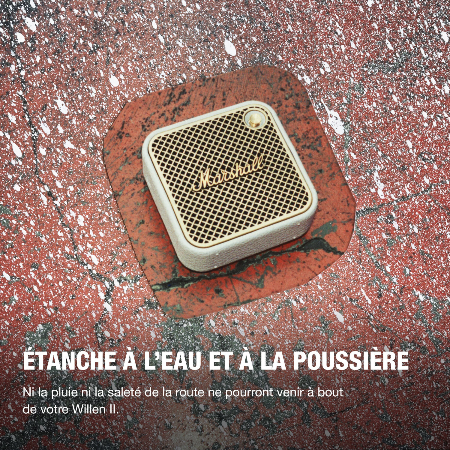 Haut-parleur Marshall blanc et doré sur une surface tachetée rouge et blanche.