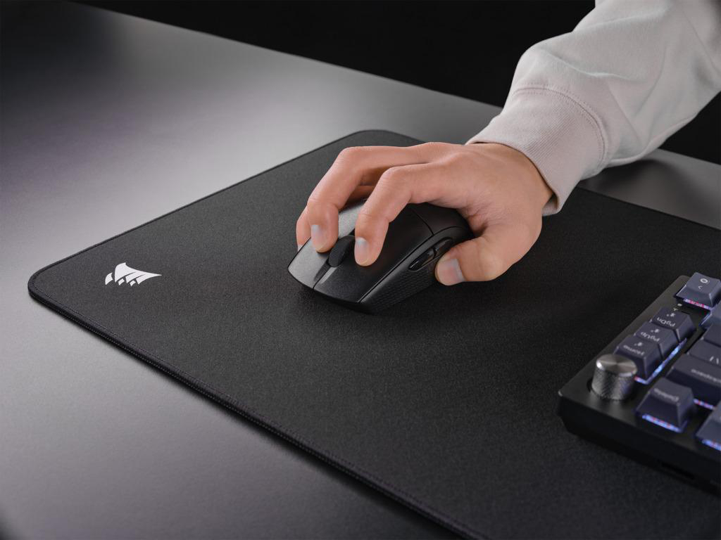 Person benutzt schwarze Corsair Maus auf schwarzem Mauspad neben Tastatur.