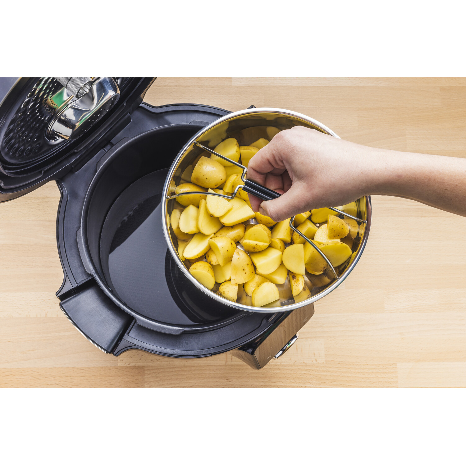 Une main soulevant un panier en acier de pommes de terre d'un pot ouvert rempli d'eau. Le pot est noir.