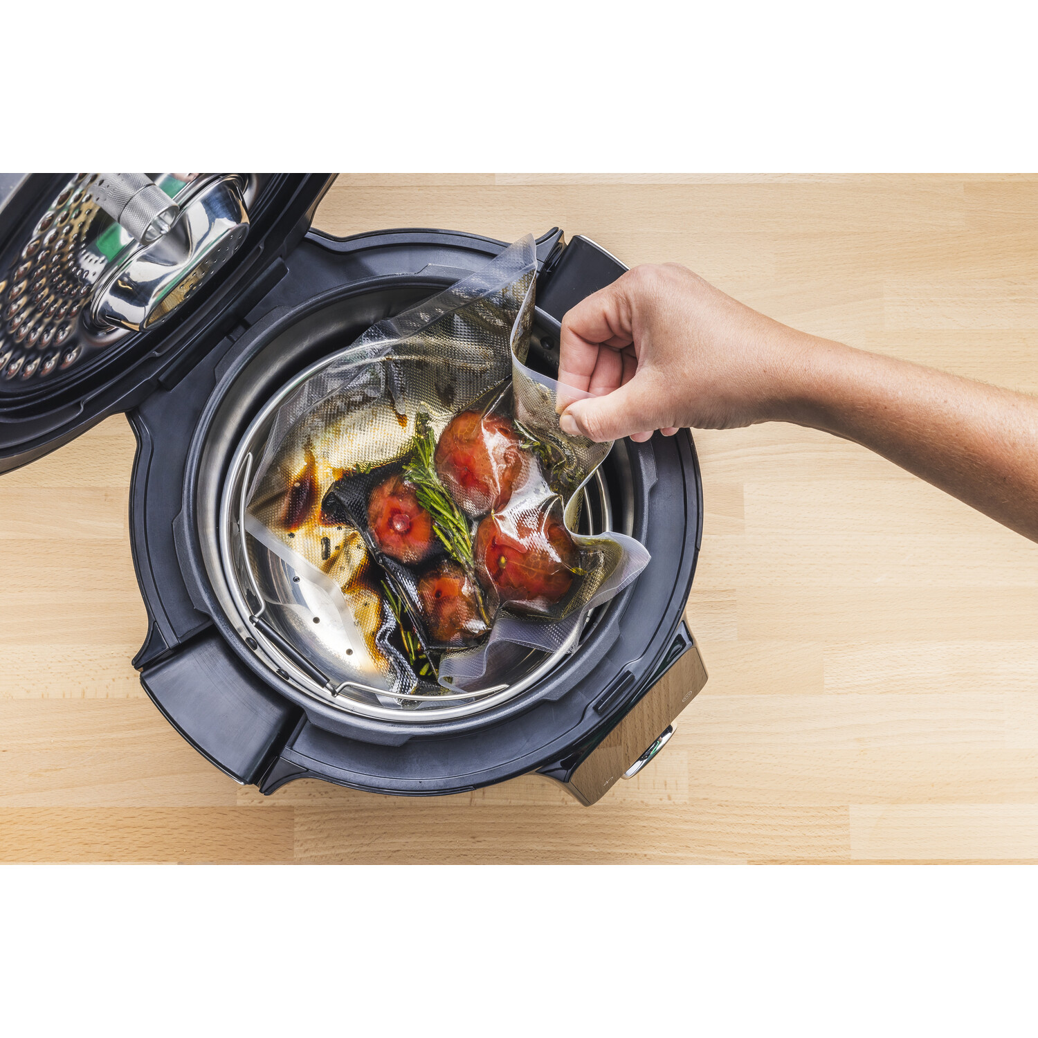 Une main plaçant un sac de légumes dans une cocotte-minute. La cocotte est noire avec un intérieur argenté.
