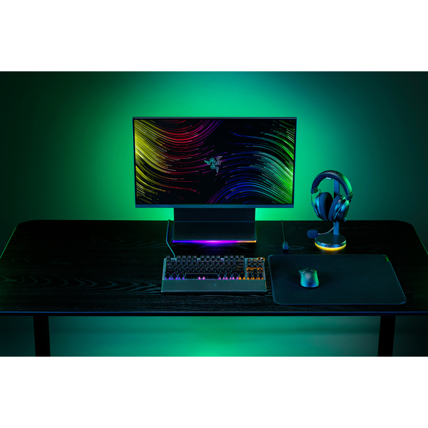 Een gaming-opstelling: toetsenbord, monitor, muis en headset op een zwart bureau met groene lichten.
