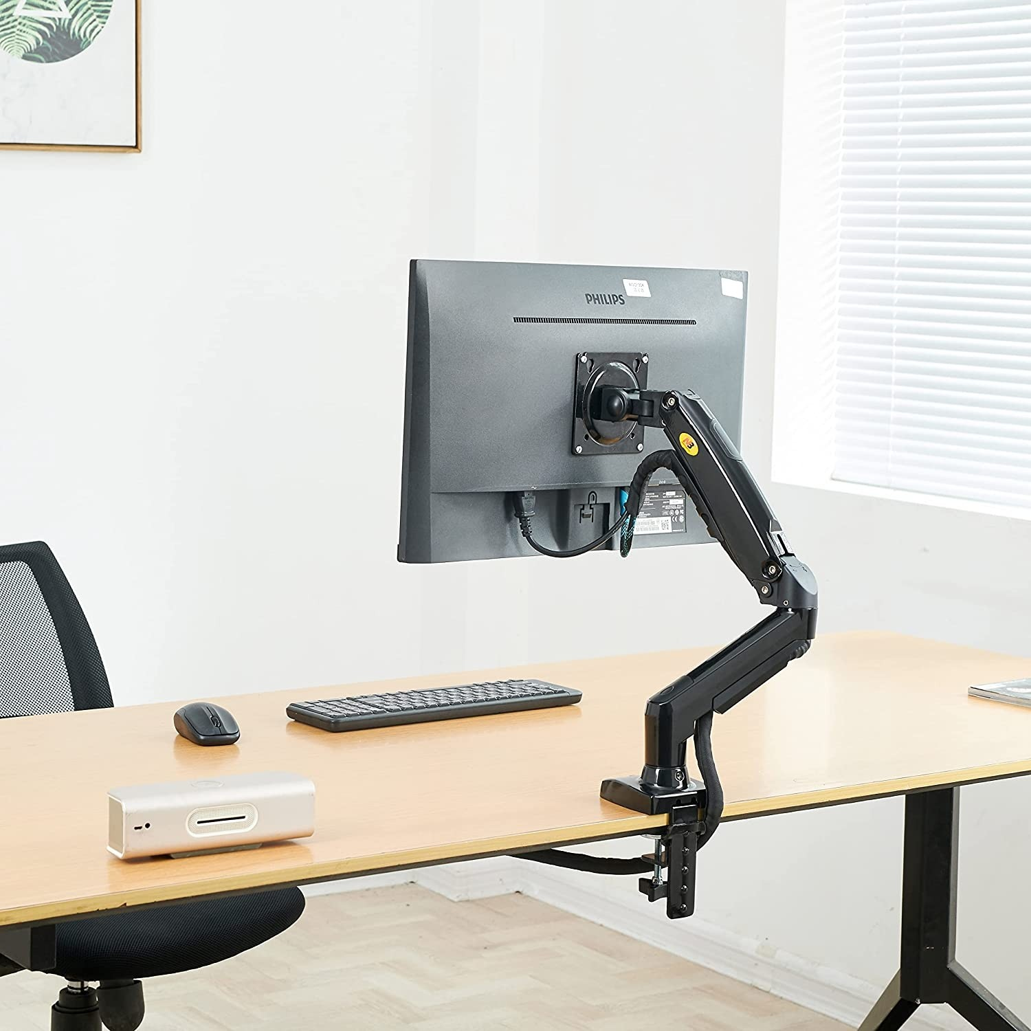 Bir masada bilgisayar monitörü. Siyah bir monitör kolu ekranı tutuyor. Klavye ve fare görülüyor.