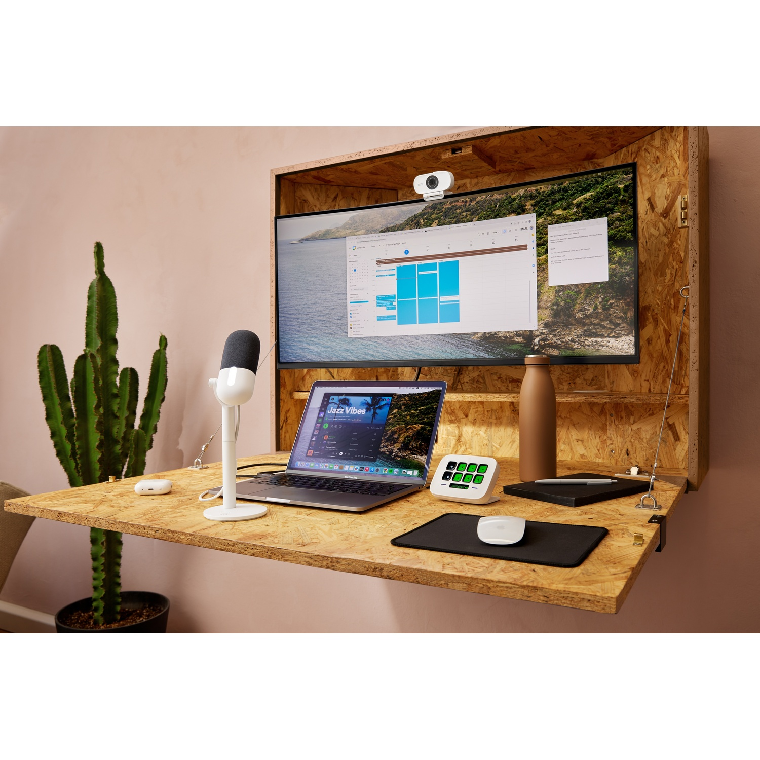 A desk with a laptop, monitor, mic, and accessories. The desk is attached to a wooden wall.