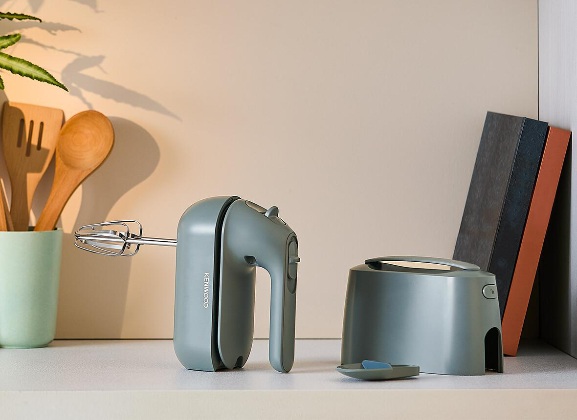 Handmixer und Zubehör auf einem Regal, mit neutralem Hintergrund.