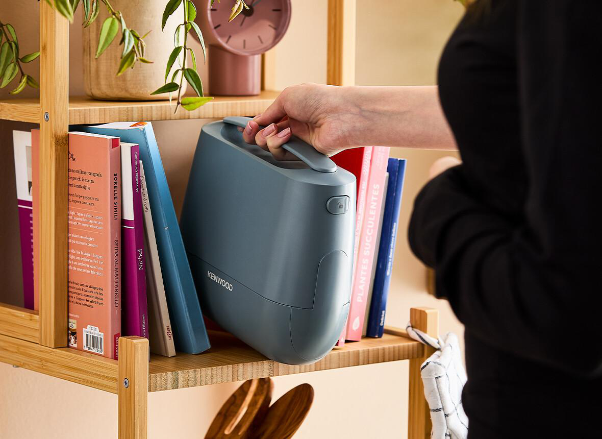 Eine Hand entfernt ein Kenwood-Gerät aus einem Regal mit Büchern und anderen Gegenständen.