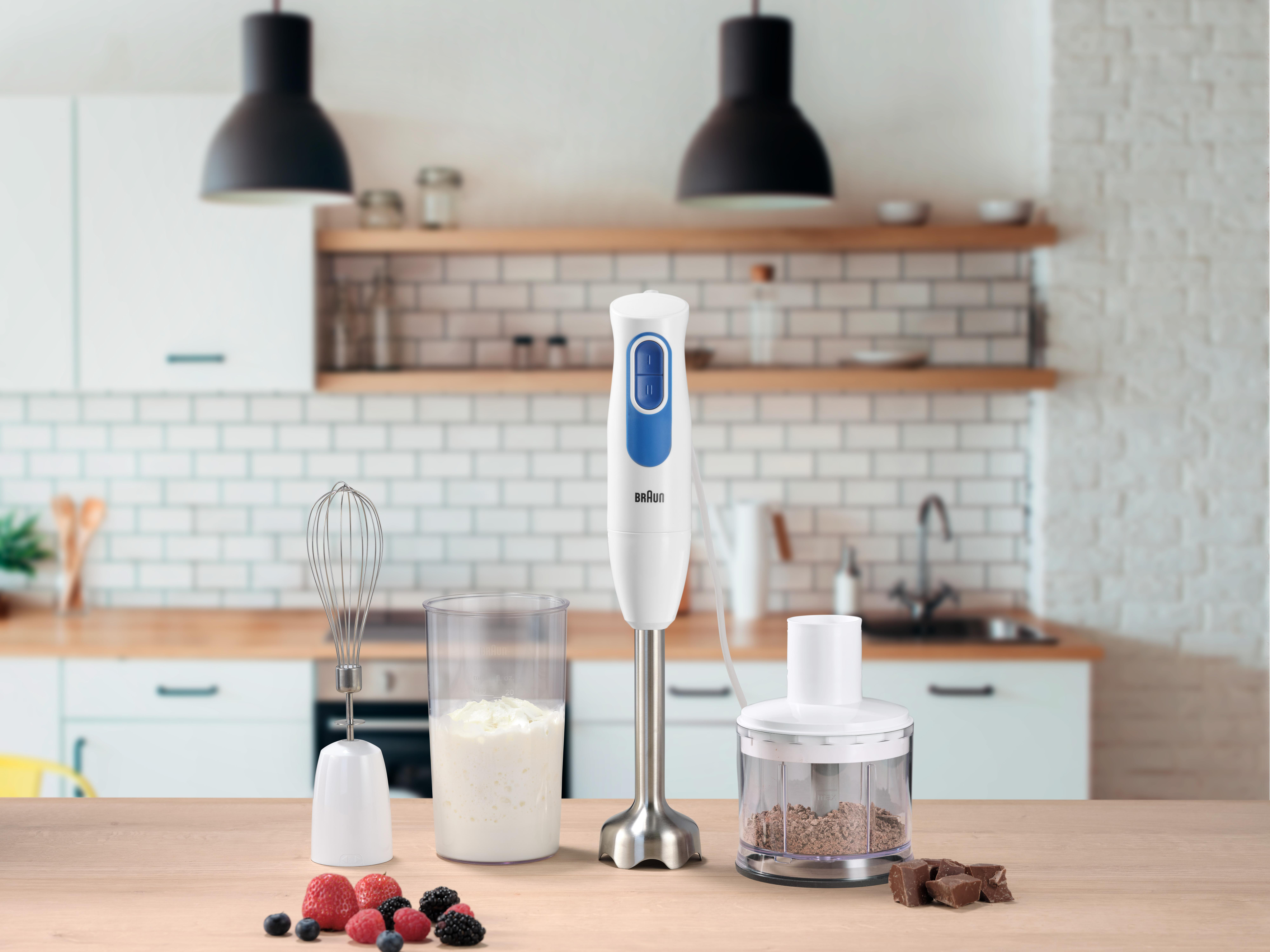 Ein weißer und blauer Handmixer, Schneebesen und Zerkleinerer mit Zutaten auf einem Tisch.