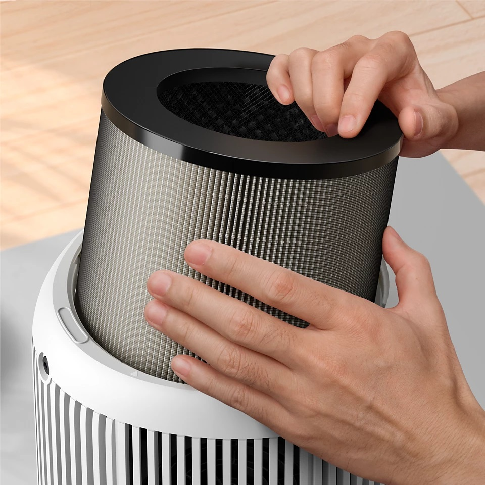 Ręce instalujące filtr powietrza w czarno-białej oczyszczaczu powietrza. Filtr jest cylindryczny.