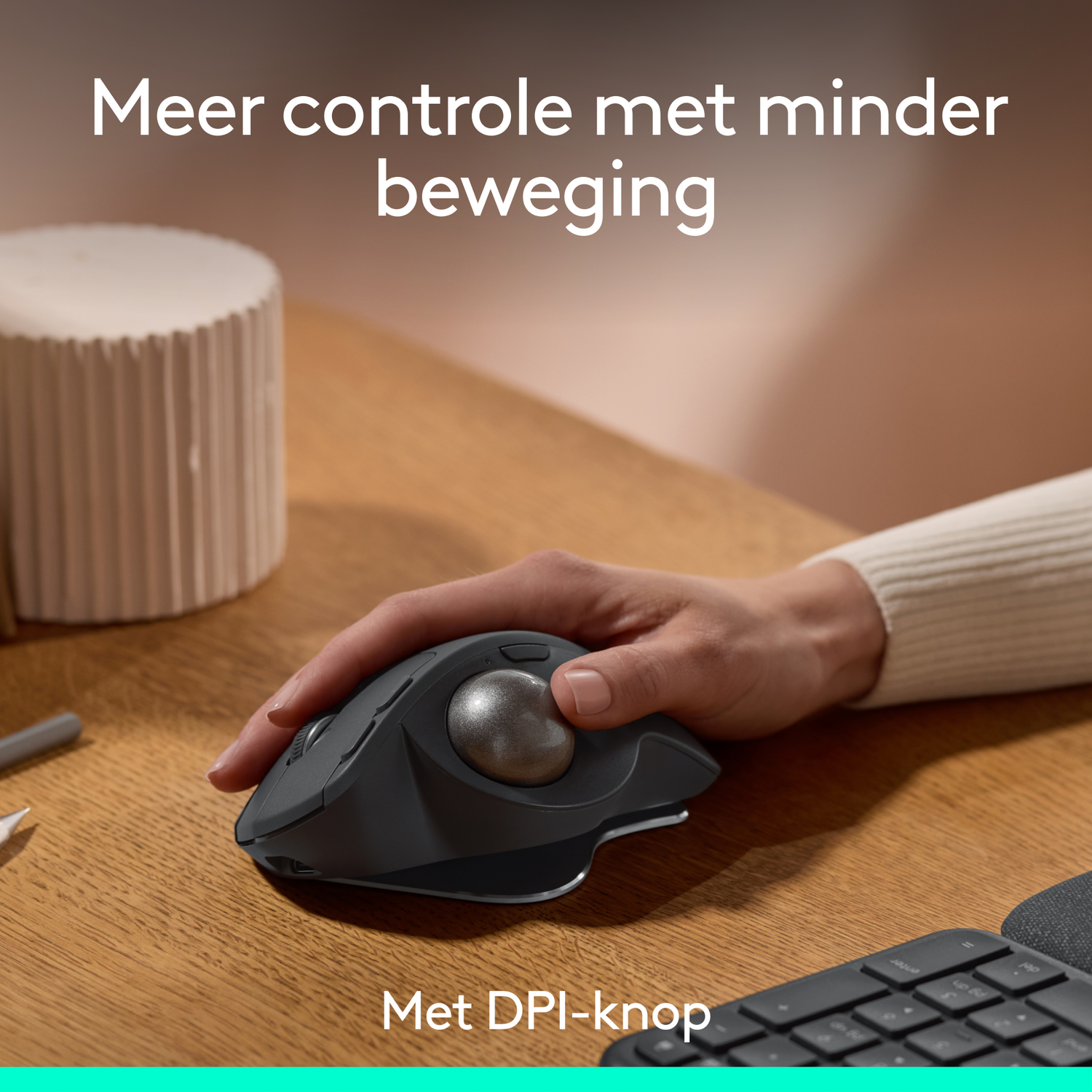 Een hand die een donkere muis met een zilveren trackball vasthoudt, op een houten bureau, met tekst erboven en eronder.