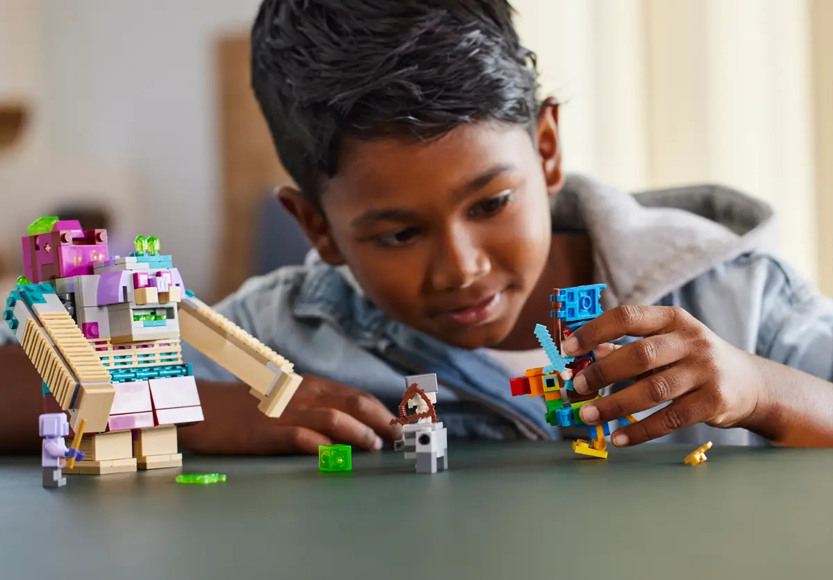 Chłopiec bawiący się figurkami Lego na stole. Widoczne są dwie figurki.