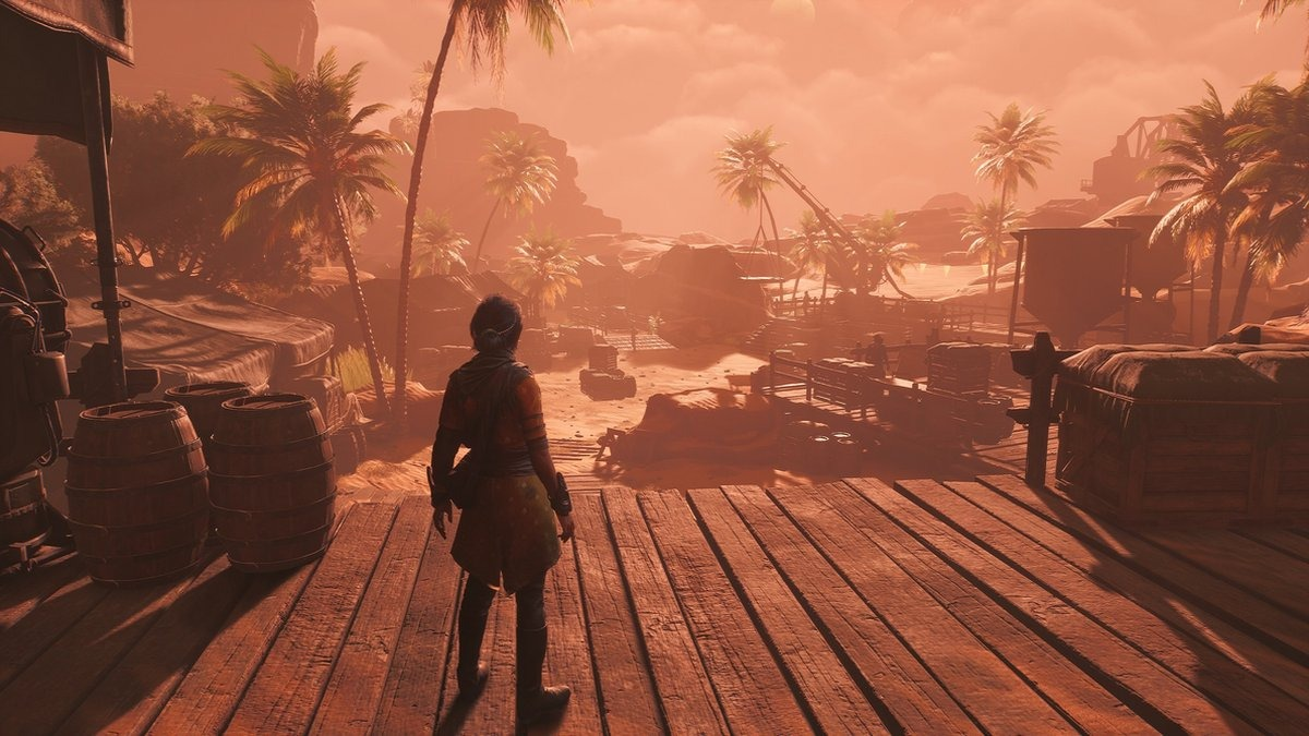 Een persoon staat op een houten pier en kijkt naar een kustplaats onder een oranje lucht.