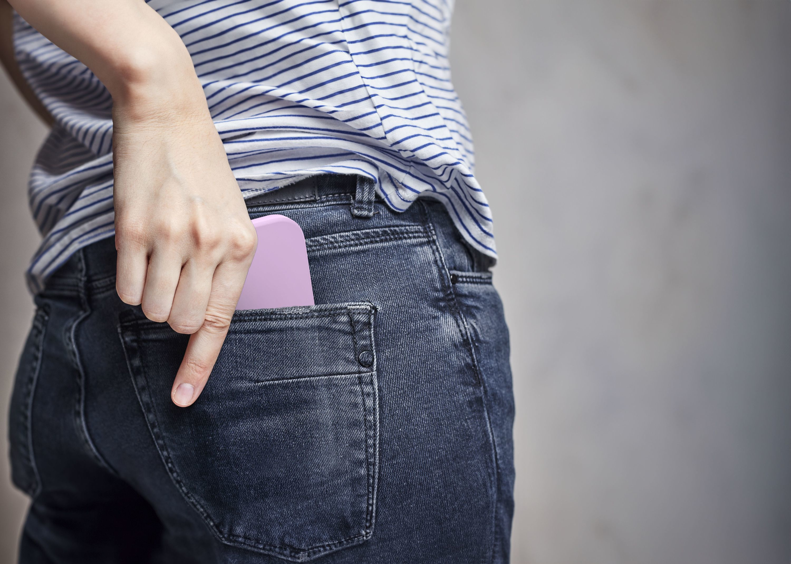 Hand steckt ein pinkes Telefon in die Gesäßtasche einer Jeans.