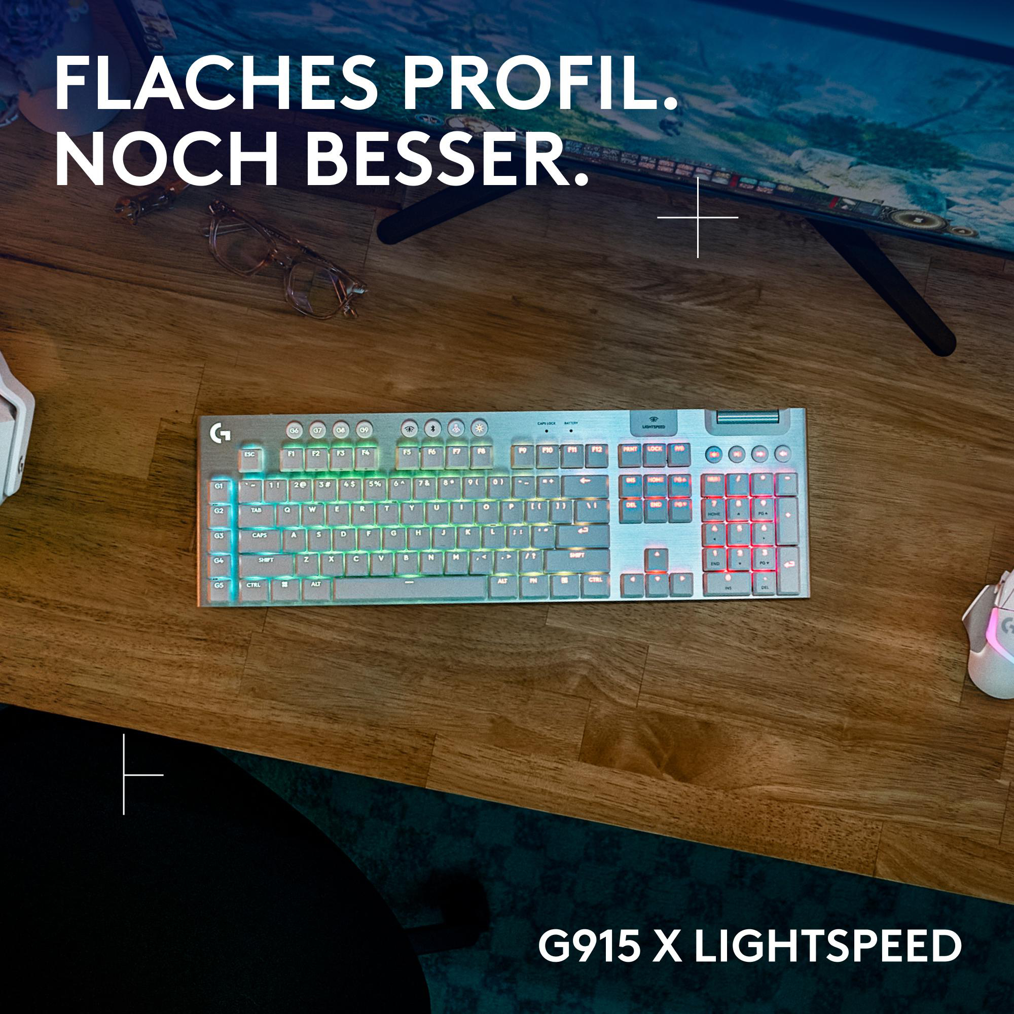 Eine silberne Tastatur auf einem Holztisch mit beleuchteten Tasten und einer kabellosen Maus.