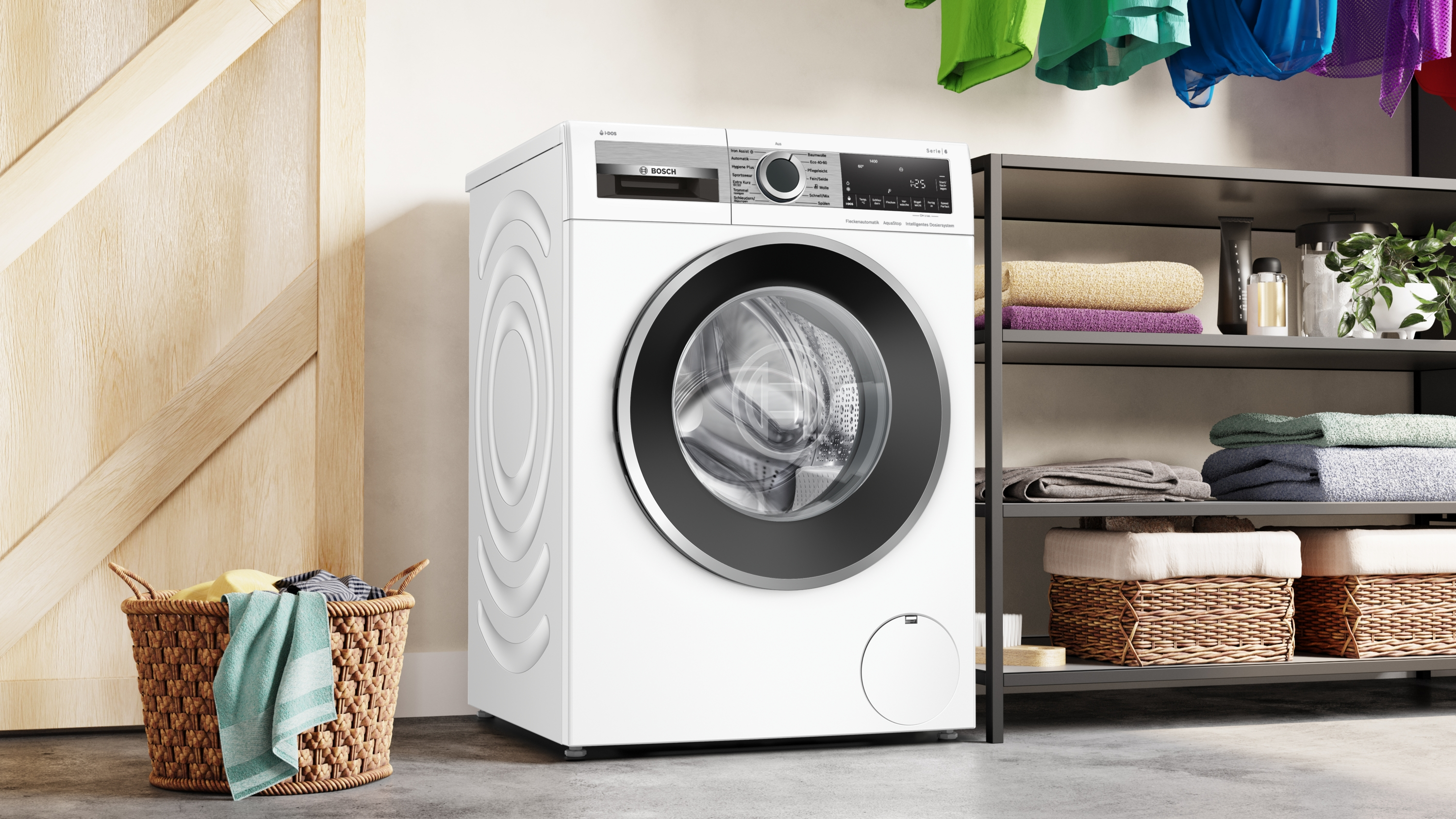 Eine weiße Waschmaschine steht neben einem Regal mit Handtüchern und Körben. Kleidung hängt darüber. Ein Korb mit Kleidung steht auf dem Boden.
