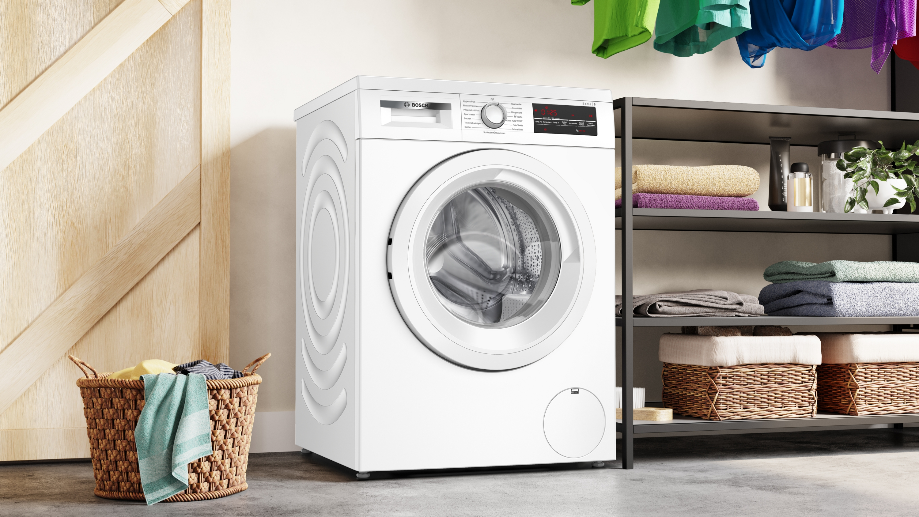 Eine weiße Waschmaschine steht neben einem Wäschekorb. Regale halten Handtücher und Reinigungsmittel. Kleidung hängt oben.