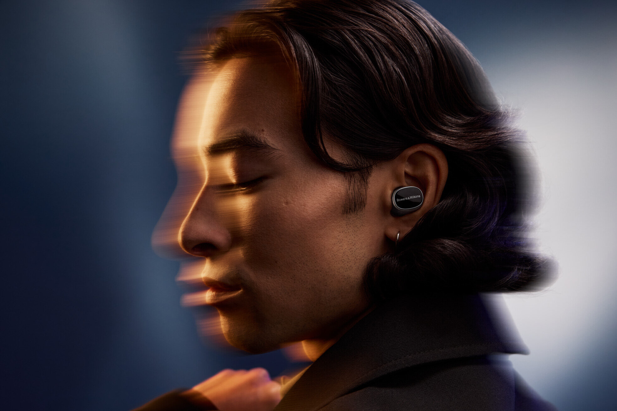 Mężczyzna w czarnych słuchawkach, rozmyte tło, prezentujący nowoczesne urządzenie audio.