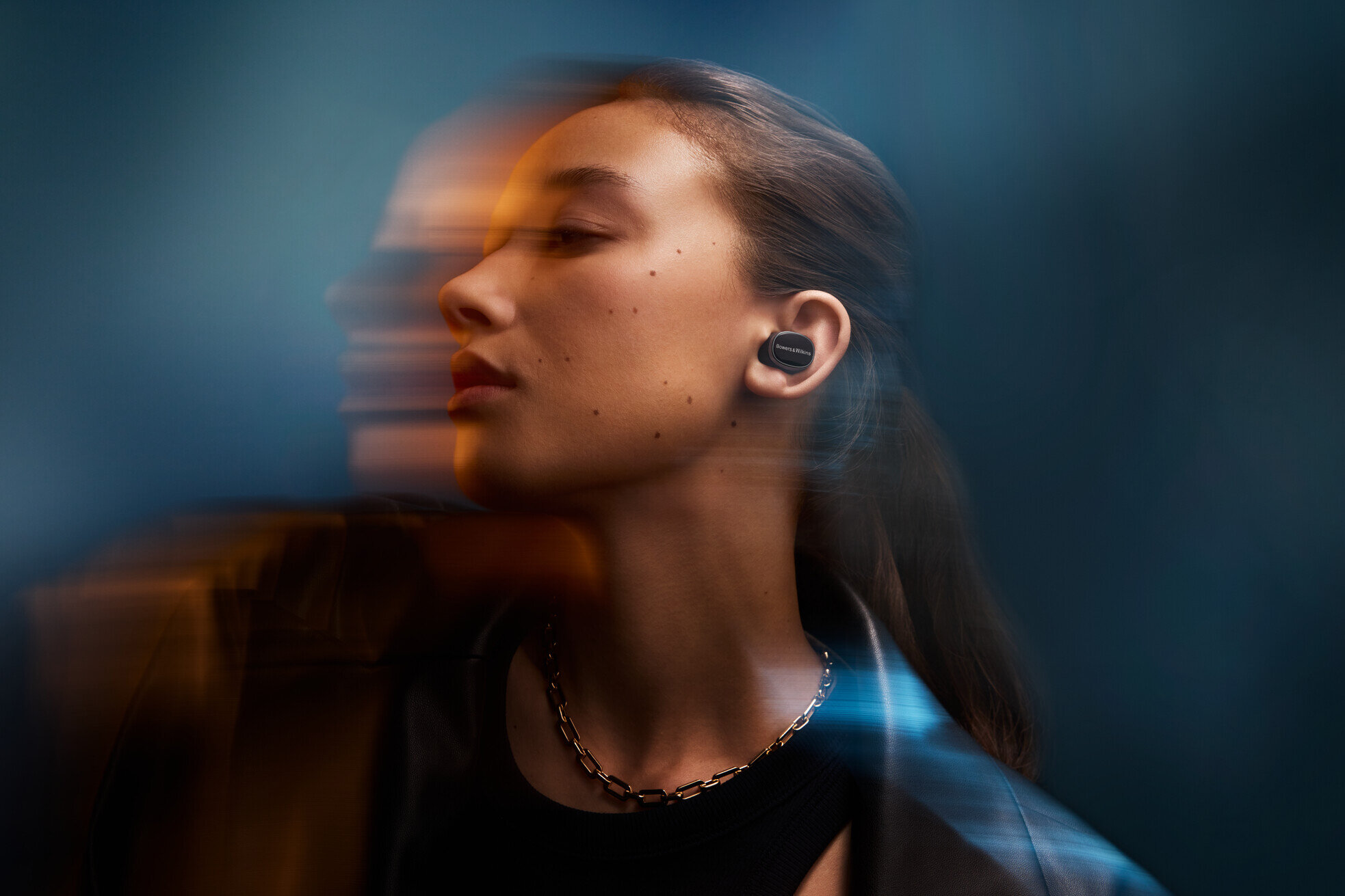 Kobieta nosząca czarne słuchawki w uchu, z naszyjnikiem.