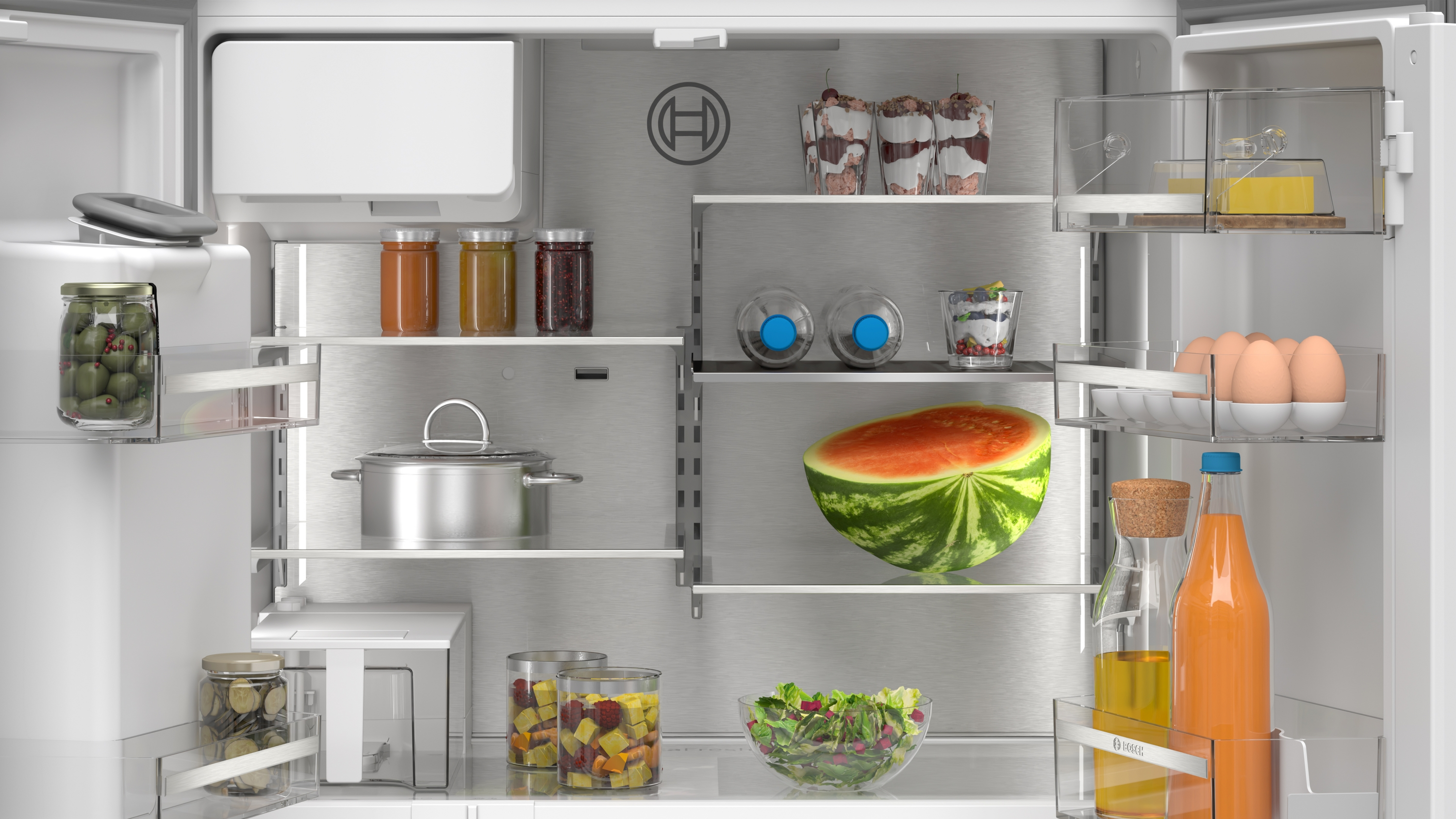 In einem Kühlschrank befinden sich verschiedene Lebensmittel: Wassermelone, Salat, Gläser, Eier, Saft und Desserts. Der Kühlschrank ist sauber und gut organisiert.