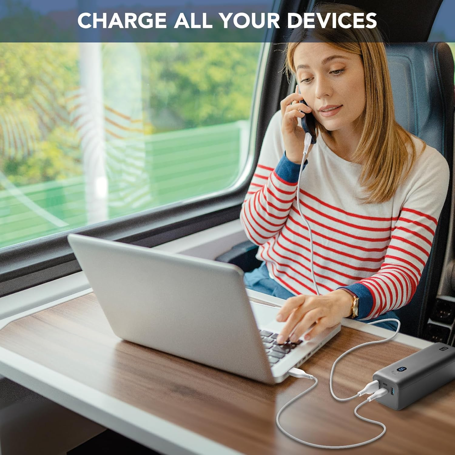Frau im Zug benutzt Laptop, verbunden mit Powerbank zum Aufladen.