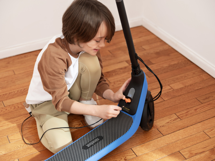 Un garçon connectant un câble de chargement à une trottinette électrique bleue et noire.