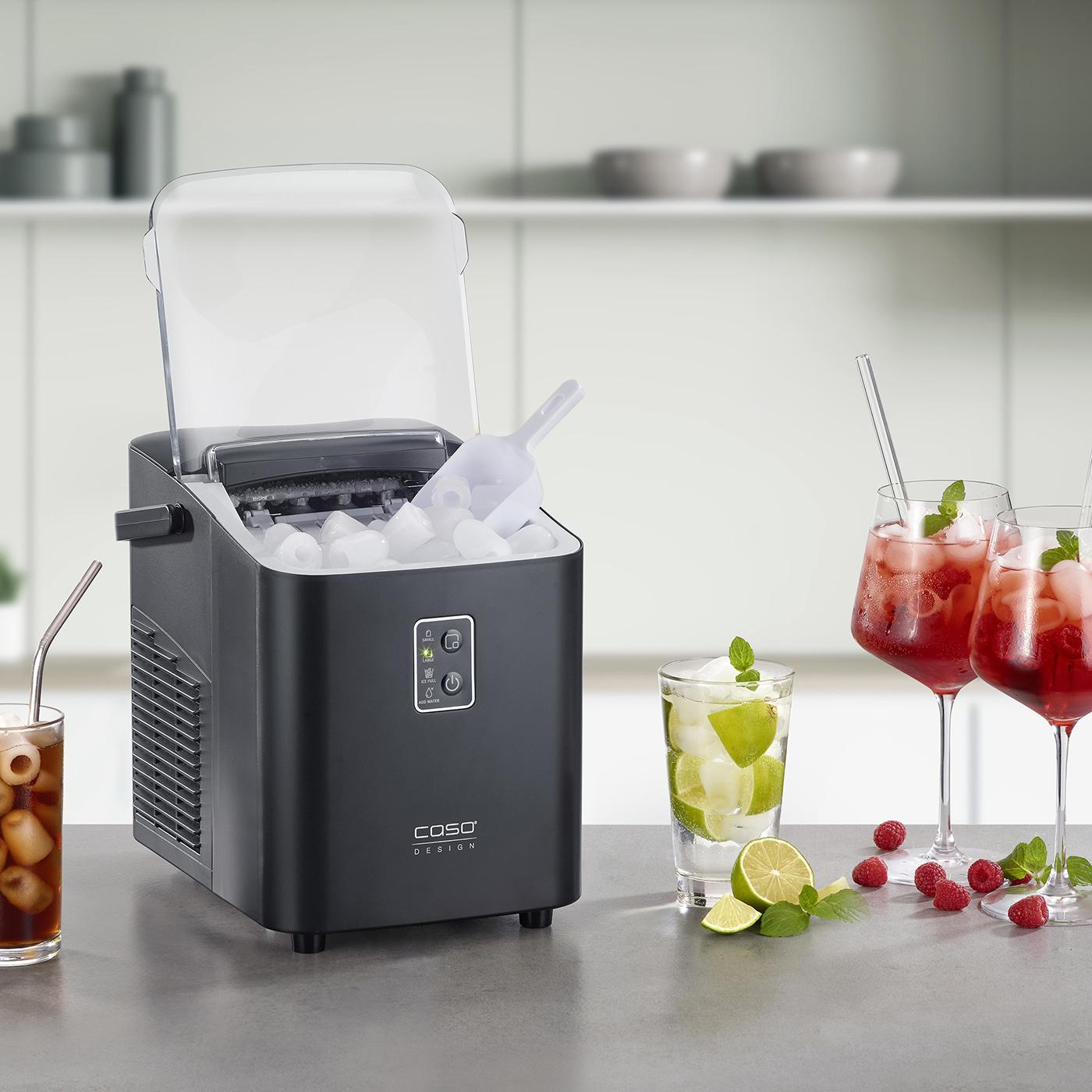 Schwarzer Eismaschine mit Eis, Schaufel, Gläsern mit Getränken und Garnierungen auf einer grauen Theke.