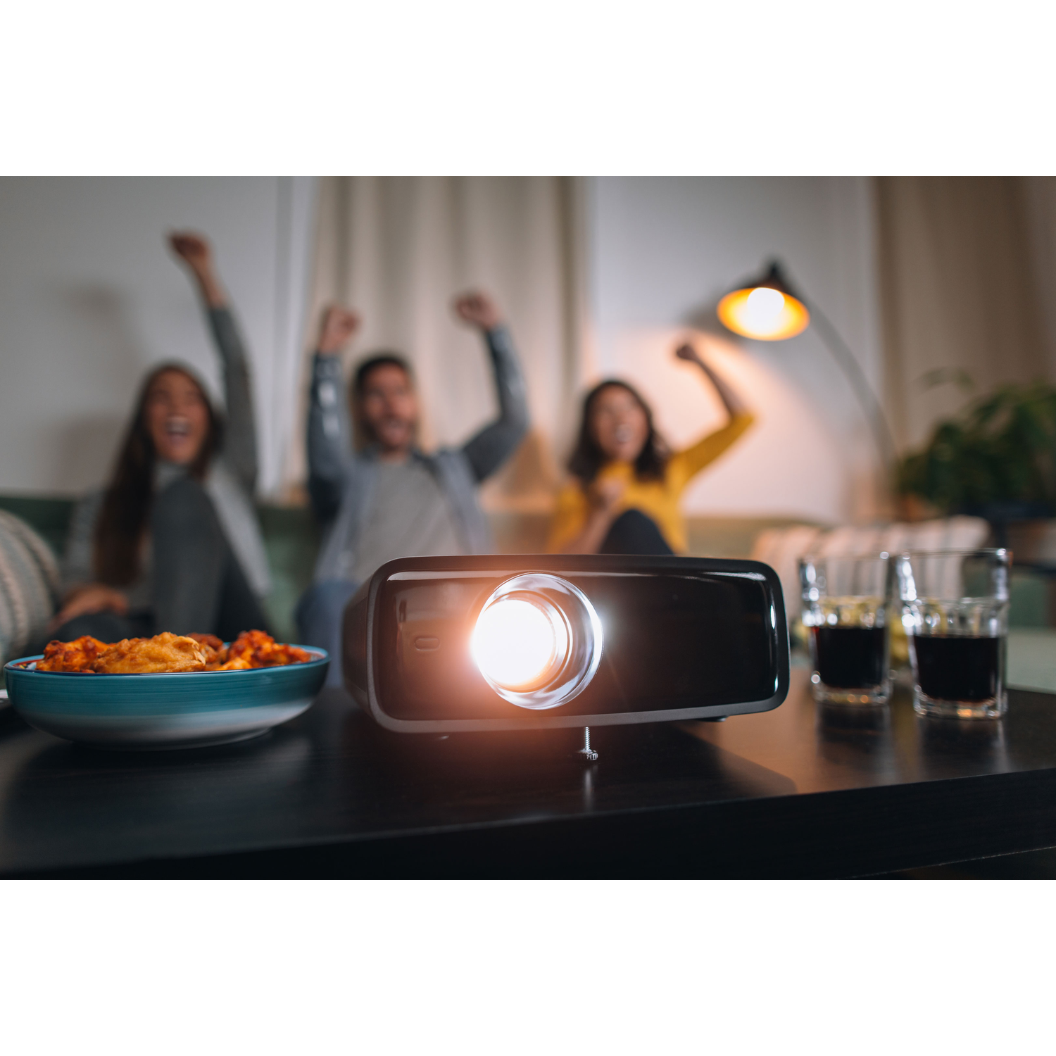 Projector projecting light onto a wall, with three people in the background cheering.