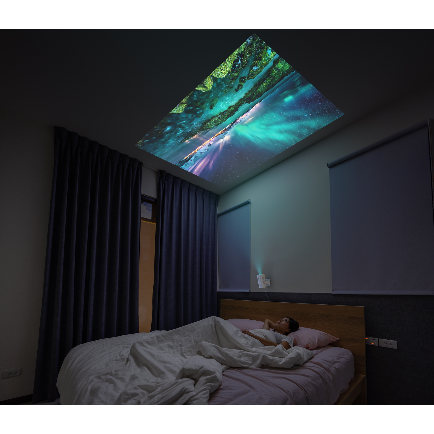 A person sleeping under a projected aurora borealis scene on the ceiling.