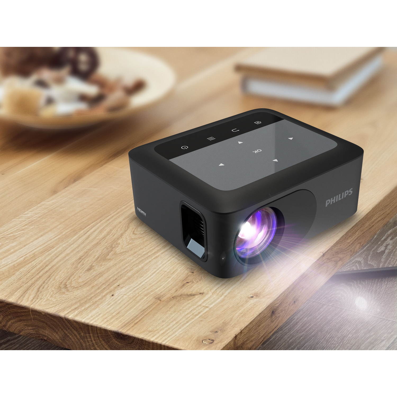 Black Philips projector, projecting light on a wooden table. Plate and book blurred in background.
