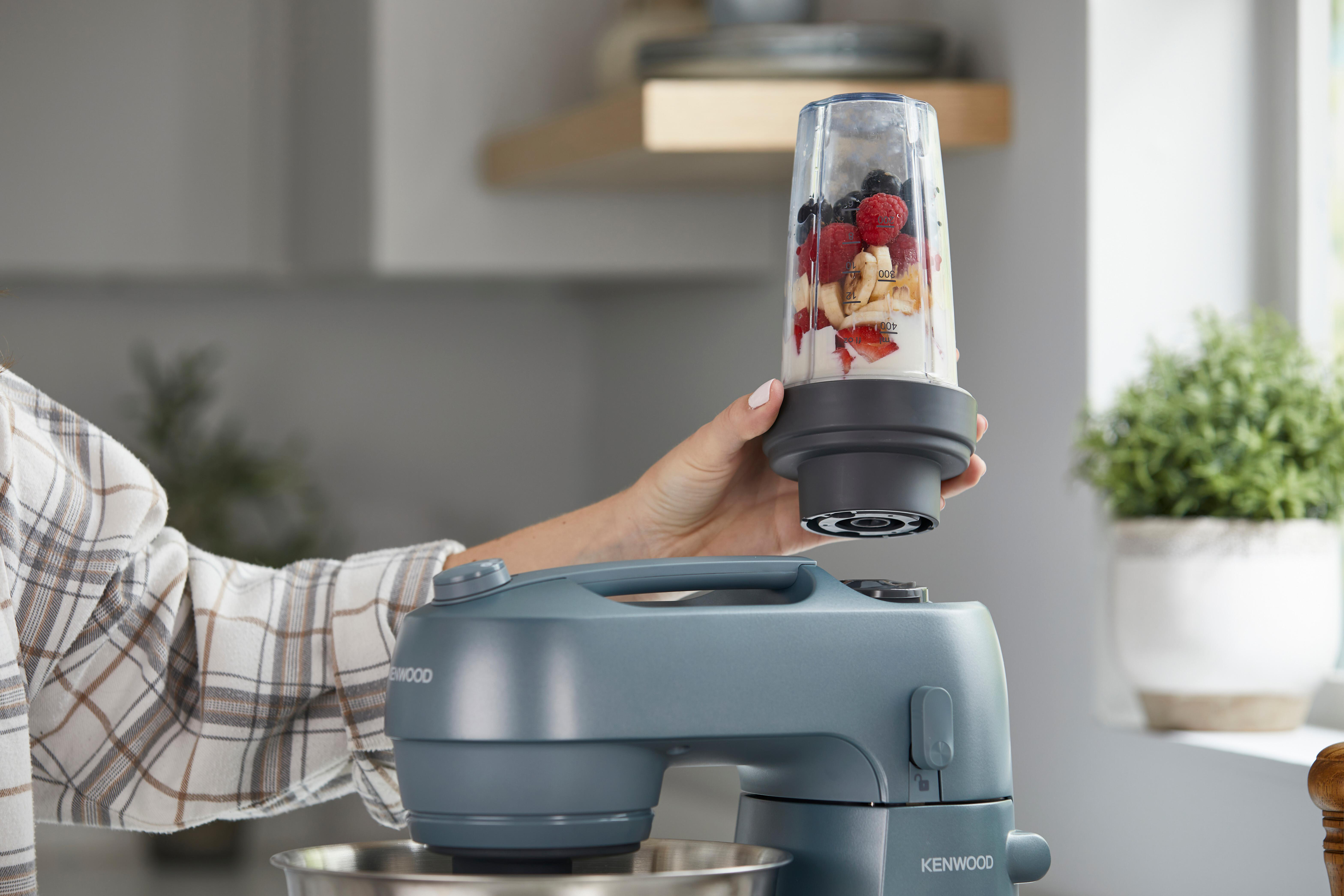 Frau hält einen mit Früchten gefüllten Mixer über eine Maschine.