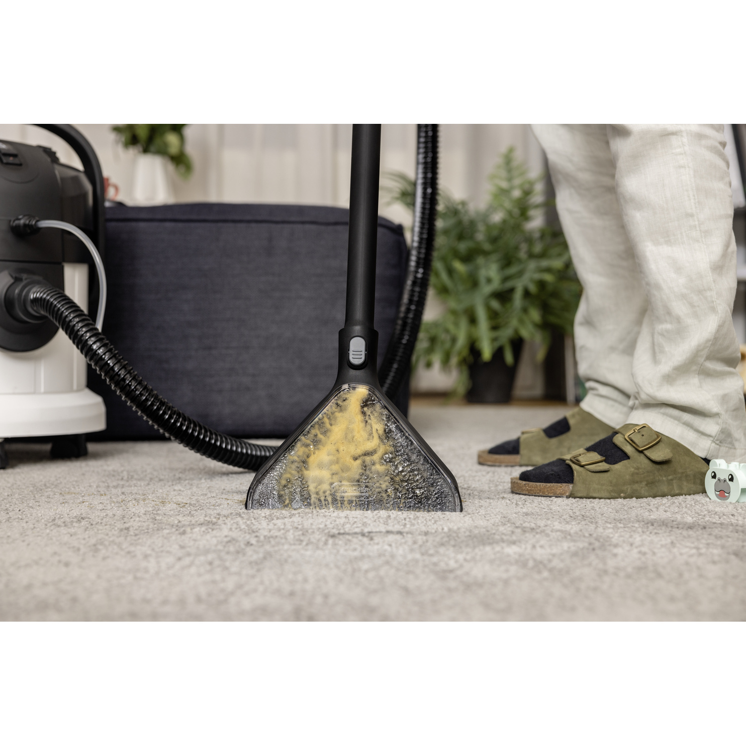 Un appareil de nettoyage de tapis en cours d'utilisation. La tête de nettoyage est sur le tapis. Une personne est en arrière-plan.