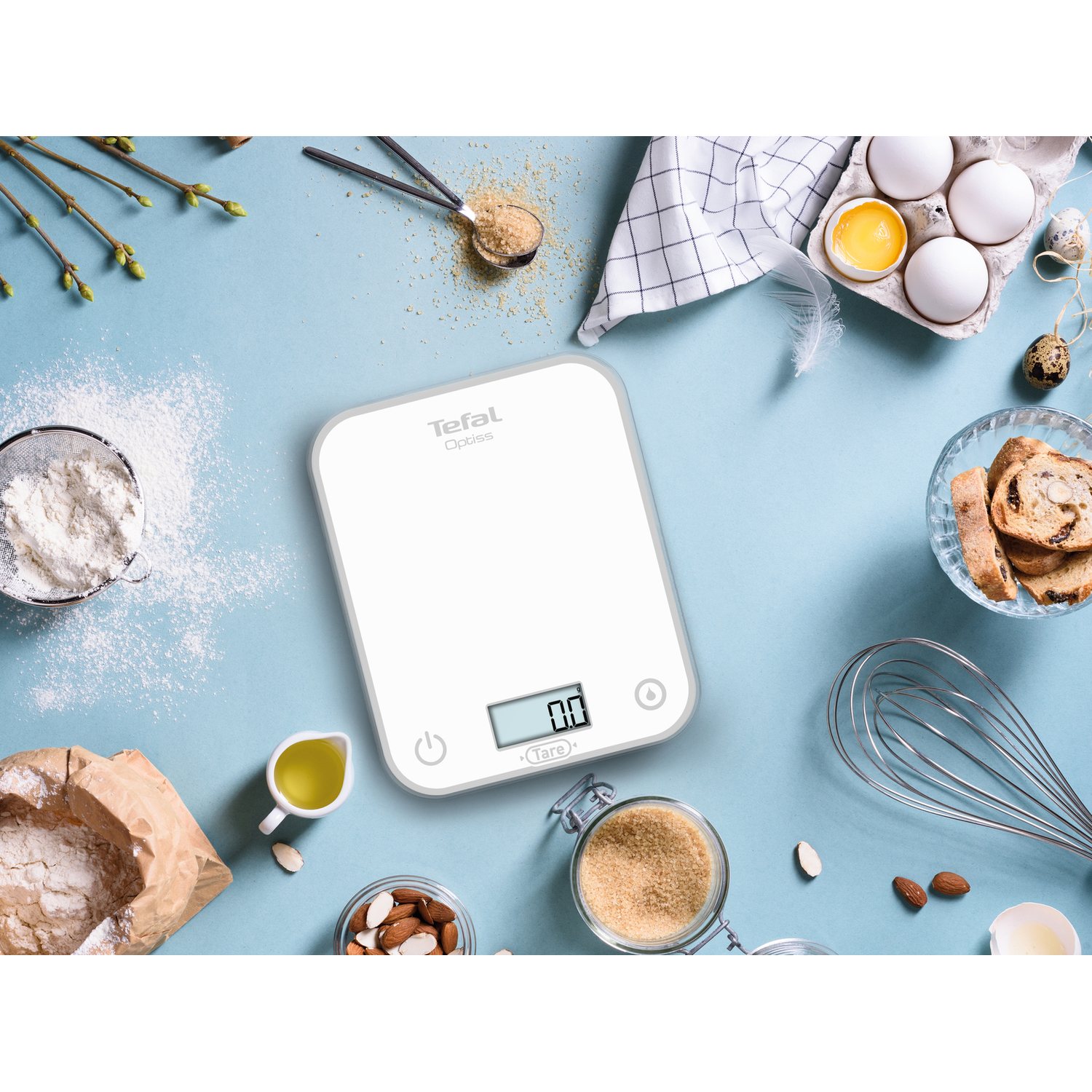 Une balance de cuisine numérique blanche avec des ingrédients autour.