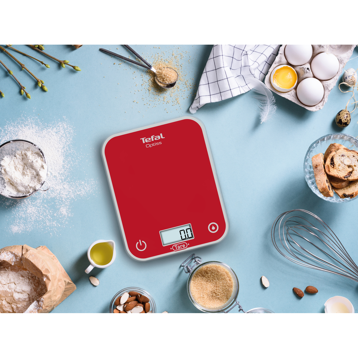 Balance de cuisine numérique rouge avec ingrédients sur une surface bleue.