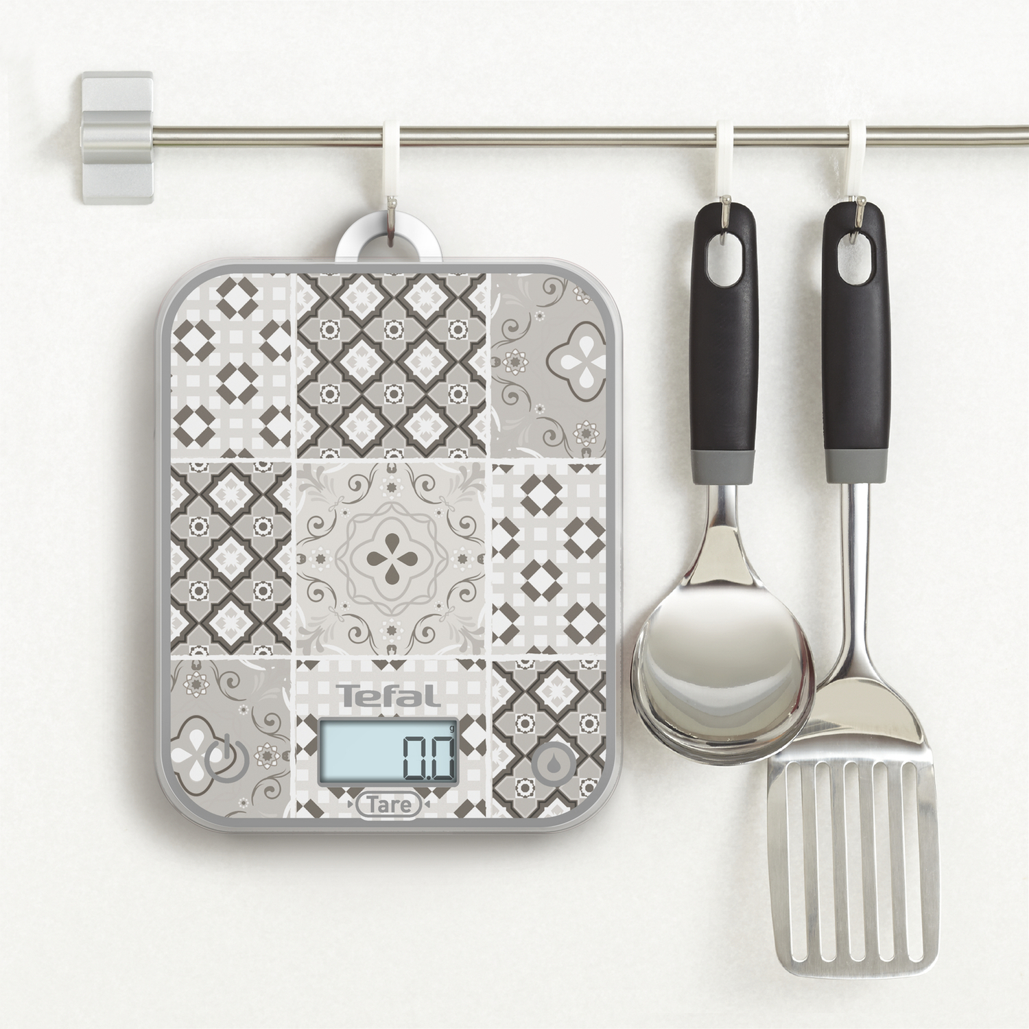 Une balance de cuisine avec un dessus à motifs colorés, à côté d'une cuillère et d'une spatule.