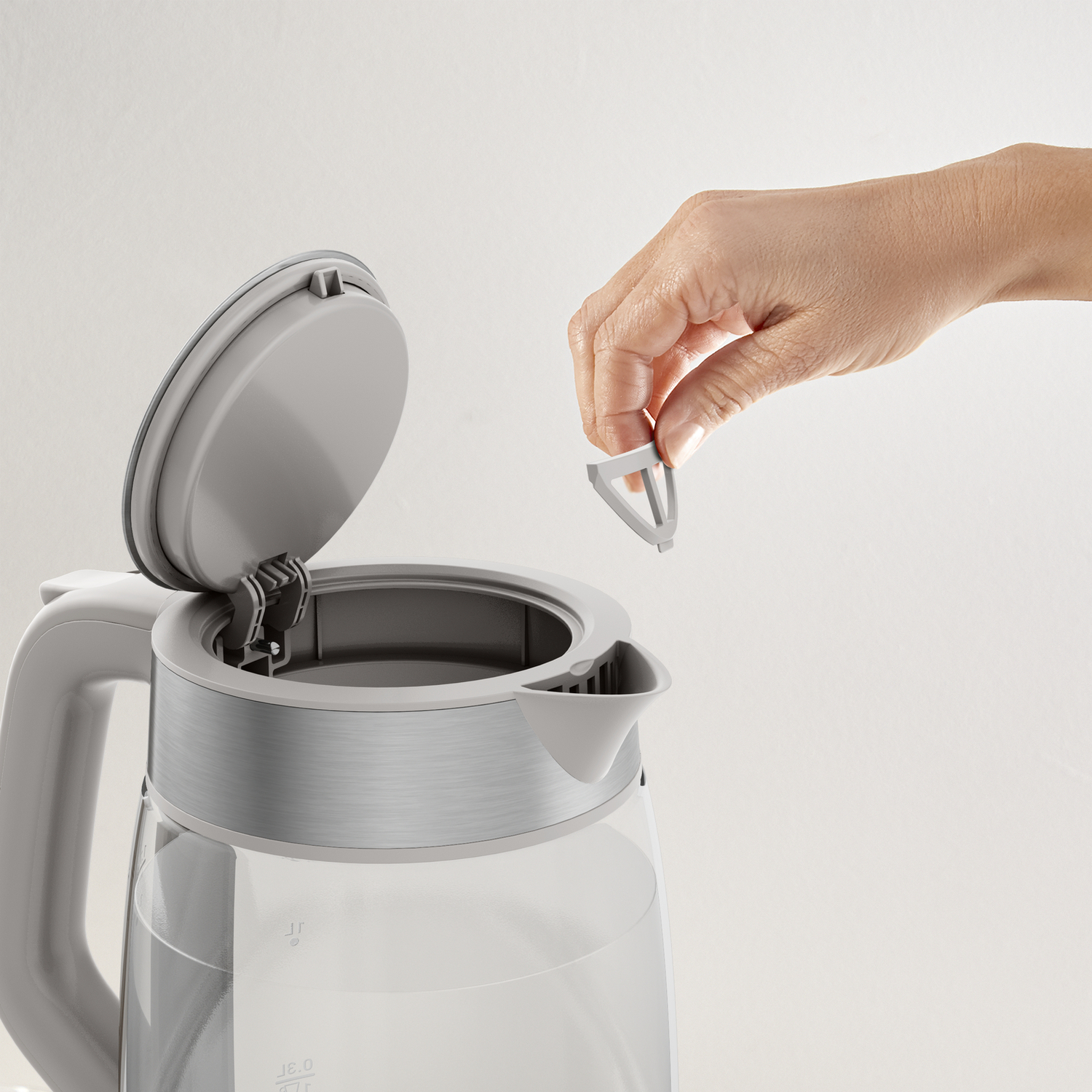 A hand placing a filter into a grey and clear electric kettle.