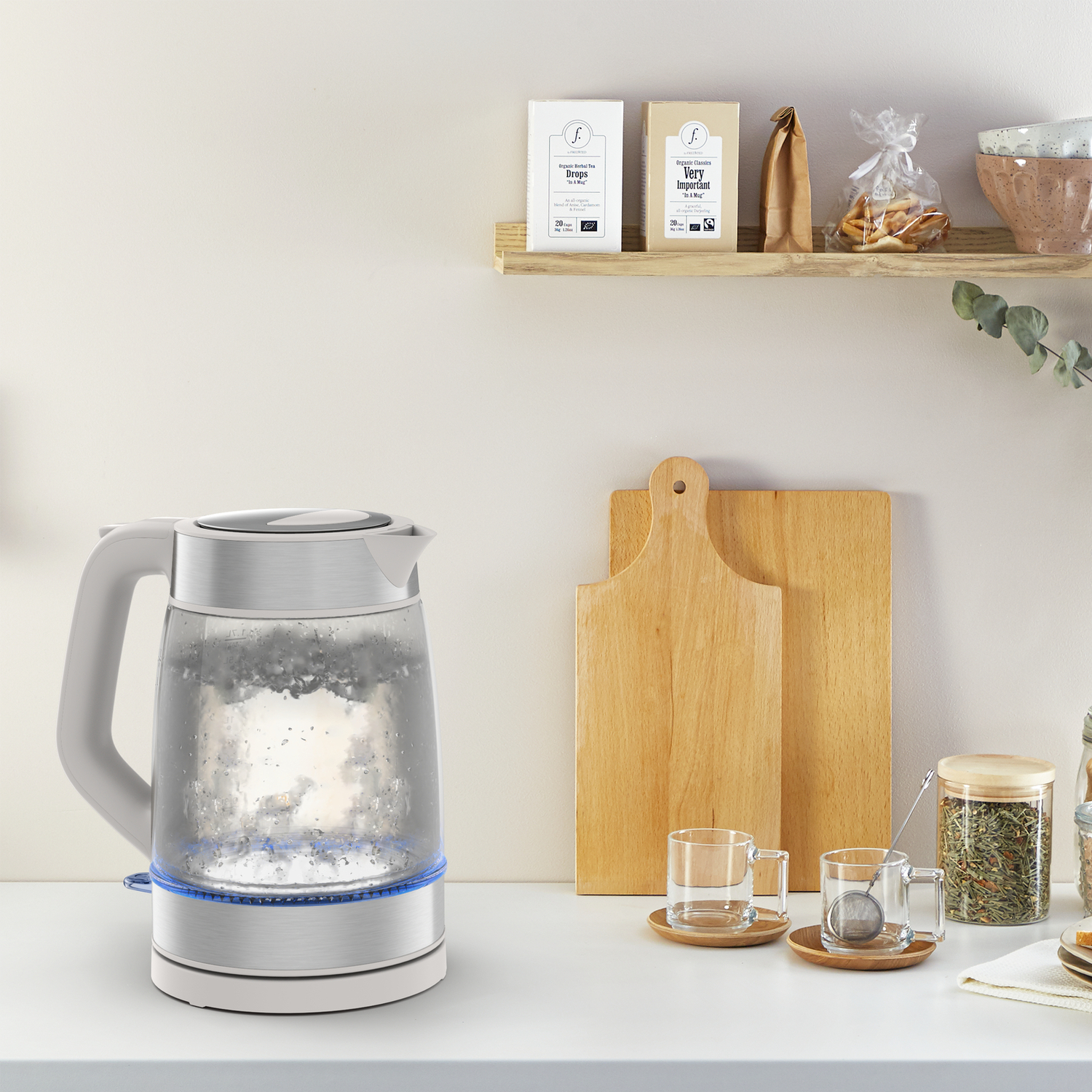 Electric kettle with water inside, set on a white surface with tea accessories.