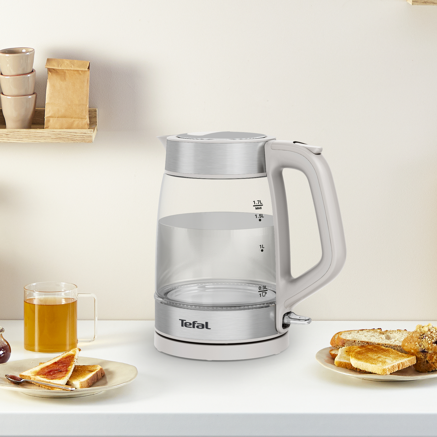 Tefal glass kettle with water inside, bread and jam on a table next to a cup.