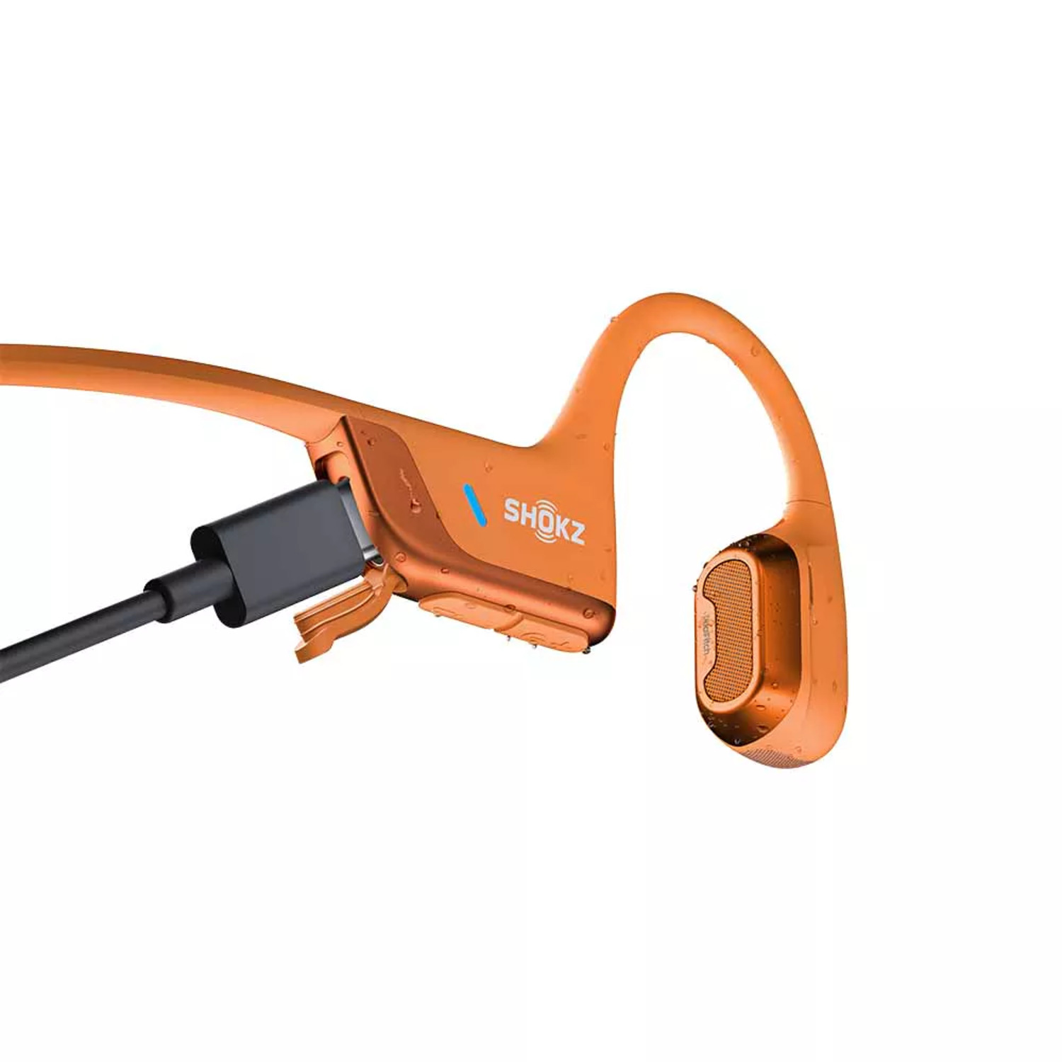 Oranje Shokz koptelefoon met oplaadkabel aangesloten op witte achtergrond.